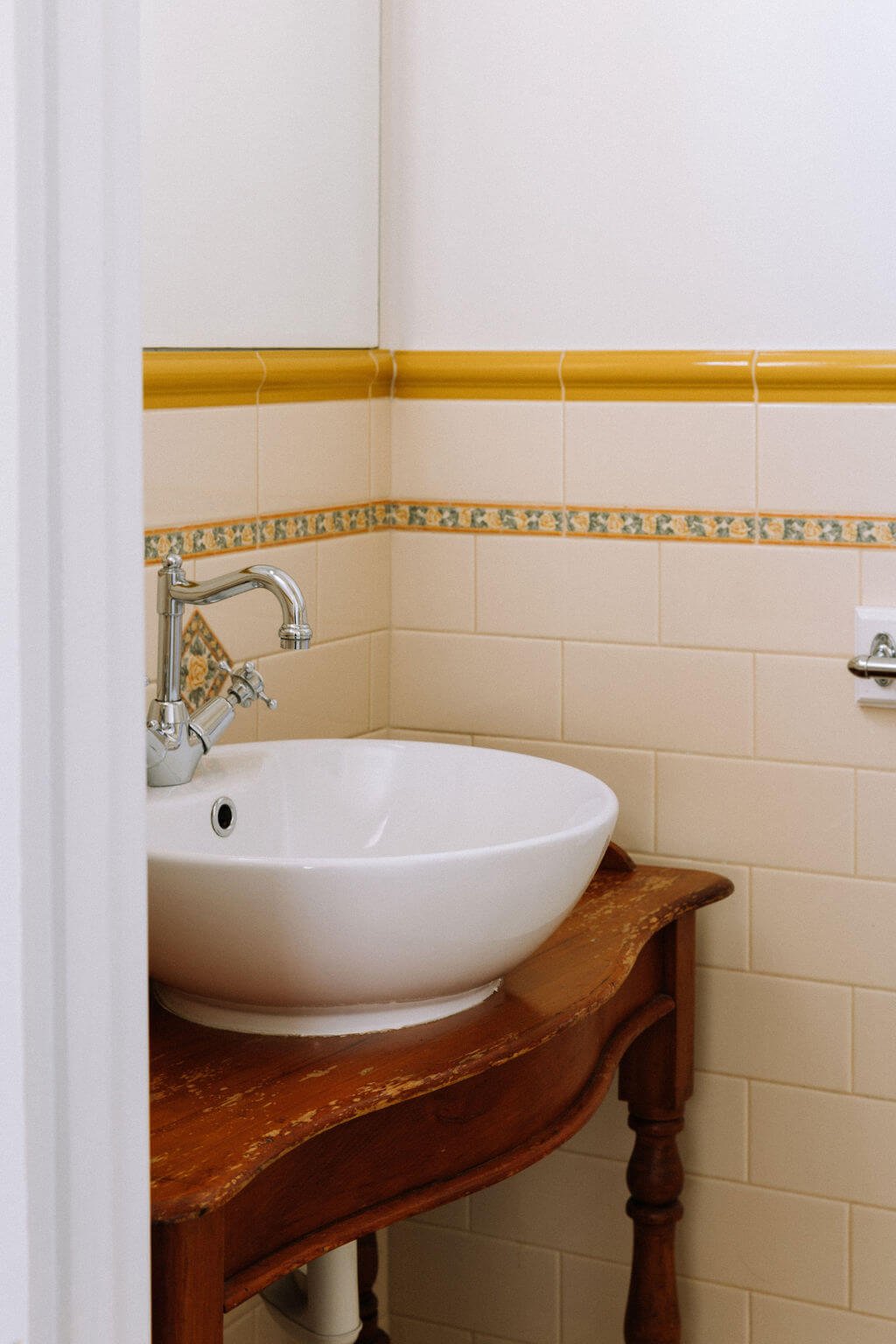 The Inn Beechworth, Luxury Accommodation - Kelly House. Bathroom corner with a white ceramic basin on a vintage wooden vanity, yellow border tiles on the walls, and a silver faucet.