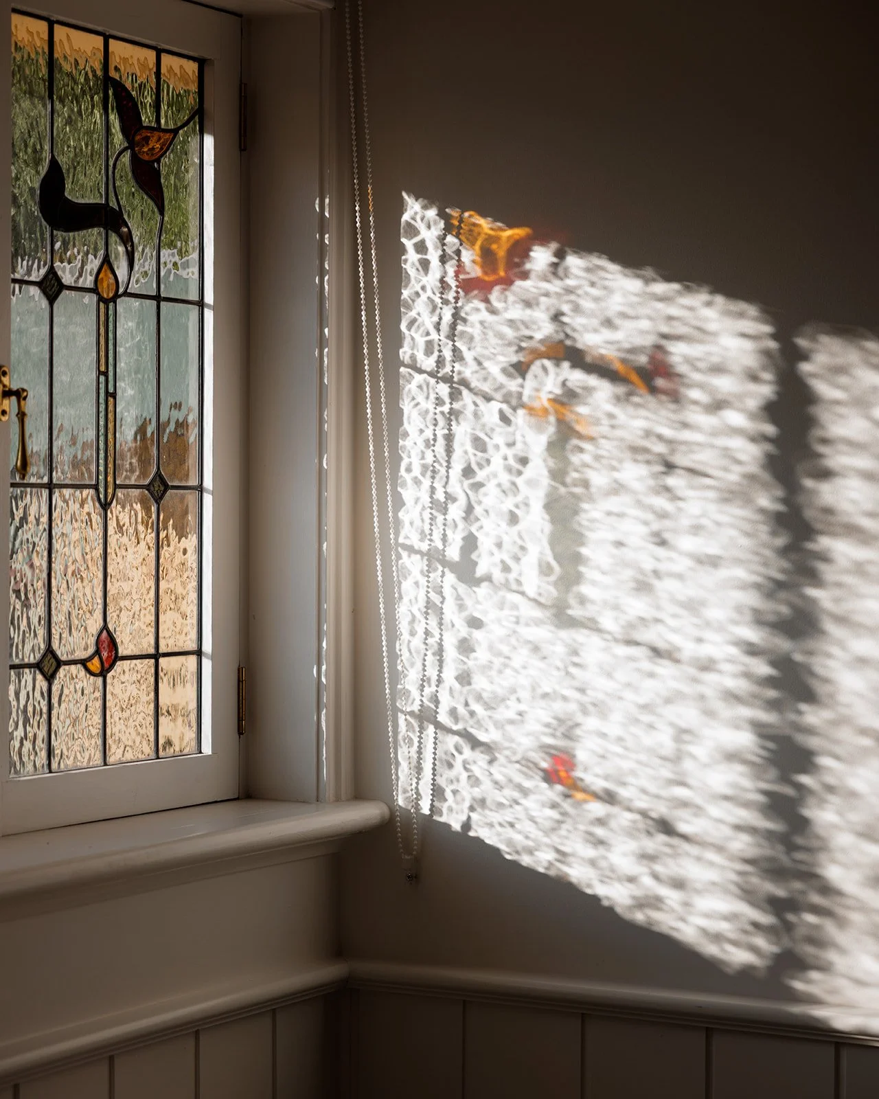 Sunlight passing through a stained glass window casting colorful reflections on a nearby wall.