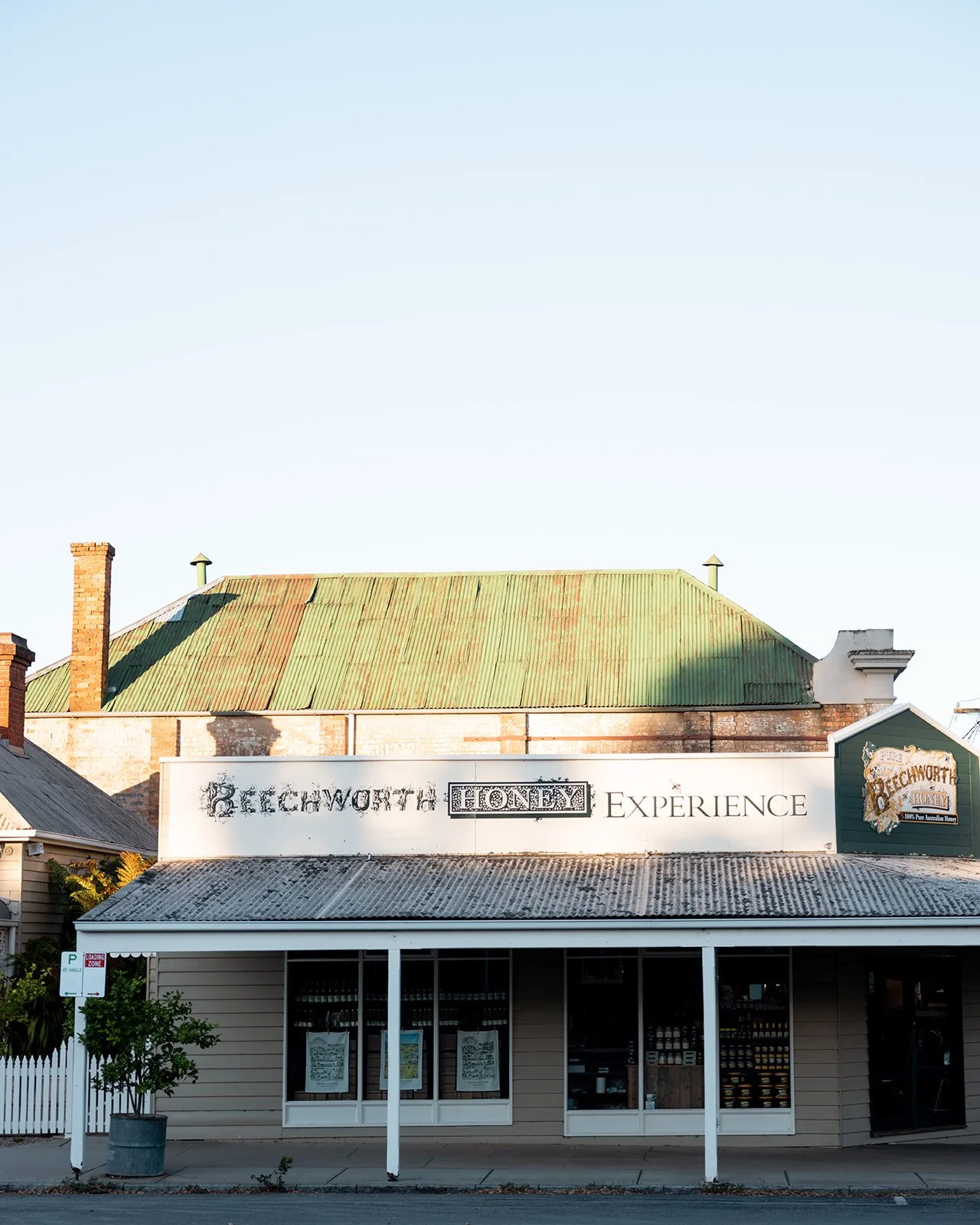 Front view of a historic building with signs reading 'Beechworth Honey Experience' and display windows.