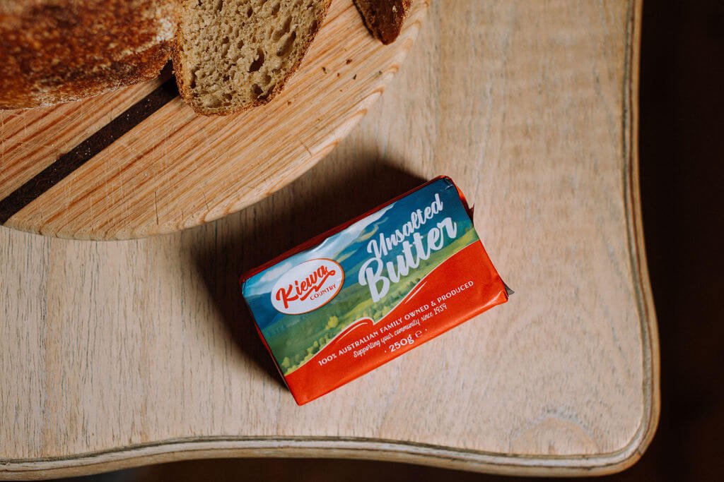 The Inn Beechworth, Luxury Accommodation - Kelly House. A partially sliced loaf of bread on a wooden cutting board next to a package of unsalted butter on a wooden table.