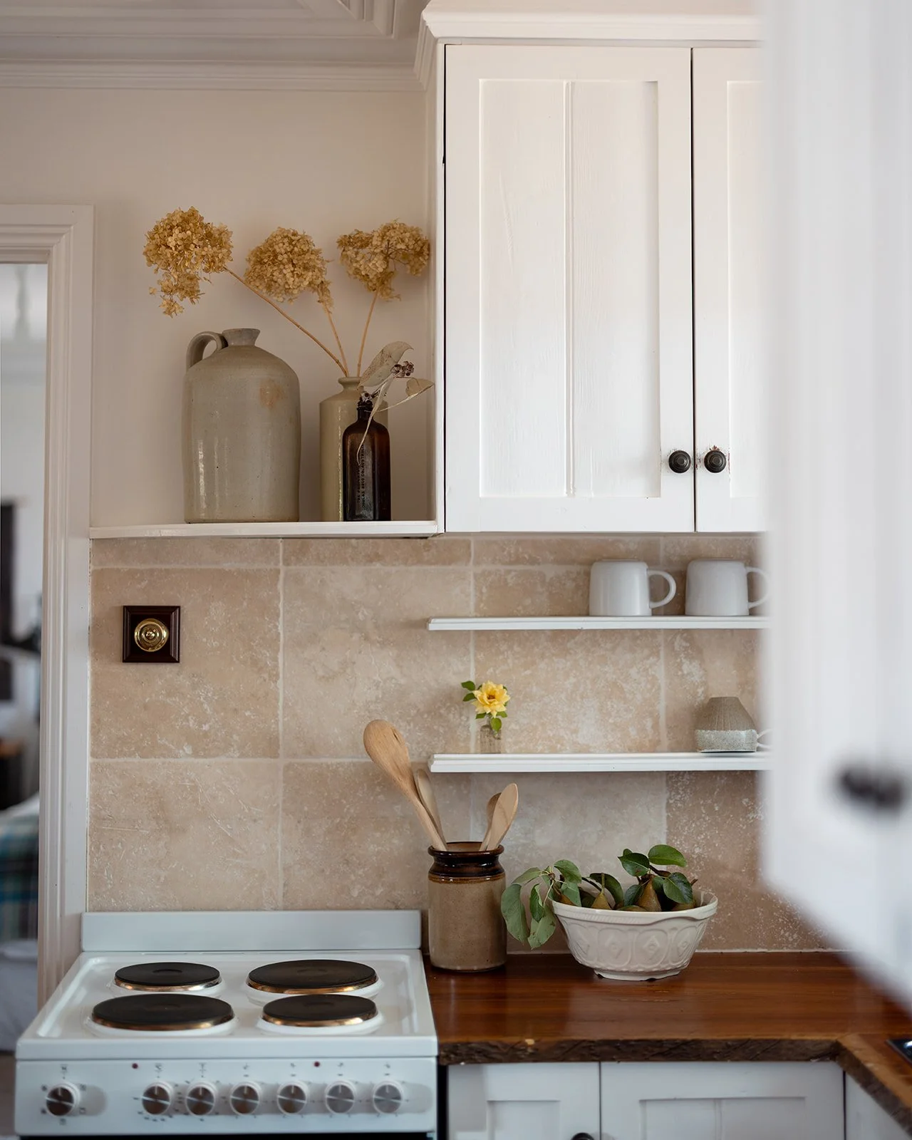 Pickett's Cottage kitchen with a white stove, wooden countertop, beige tiled backsplash, white cabinets, and decorative vases with dried flowers and a plant.
