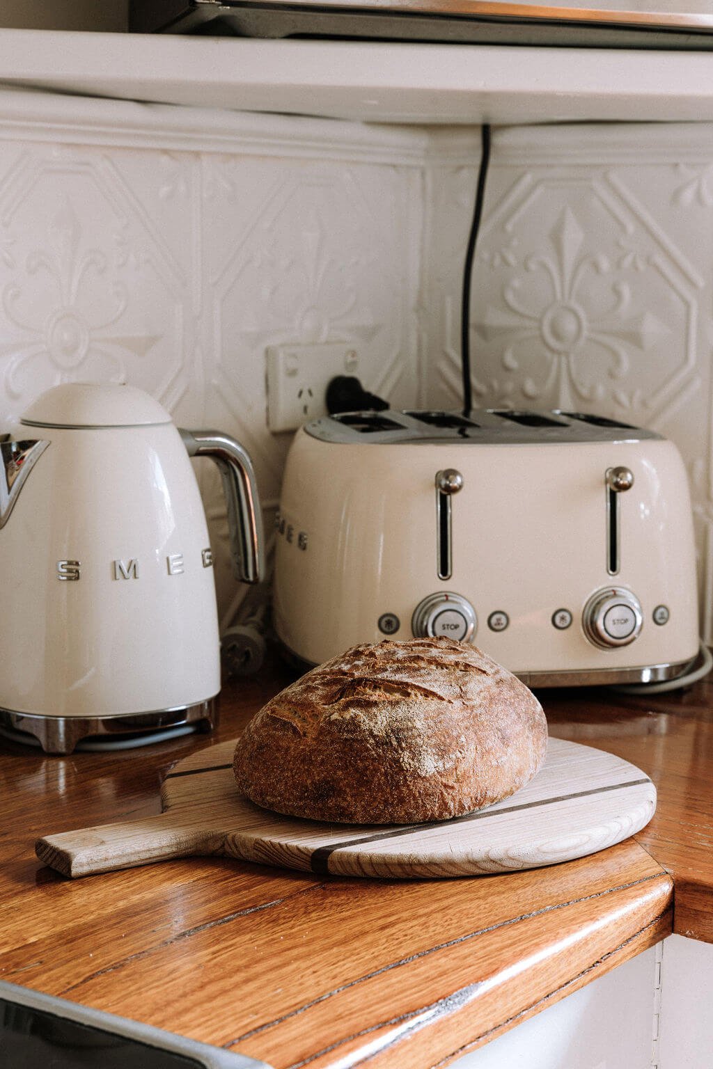 The Inn Beechworth, Luxury Accommodation - Kelly House. A kitchen scene with a loaf of bread on a wooden cutting board, next to a beige Smeg electric kettle and a Smeg four-slice toaster on a wooden countertop, with decorative tile backsplash.