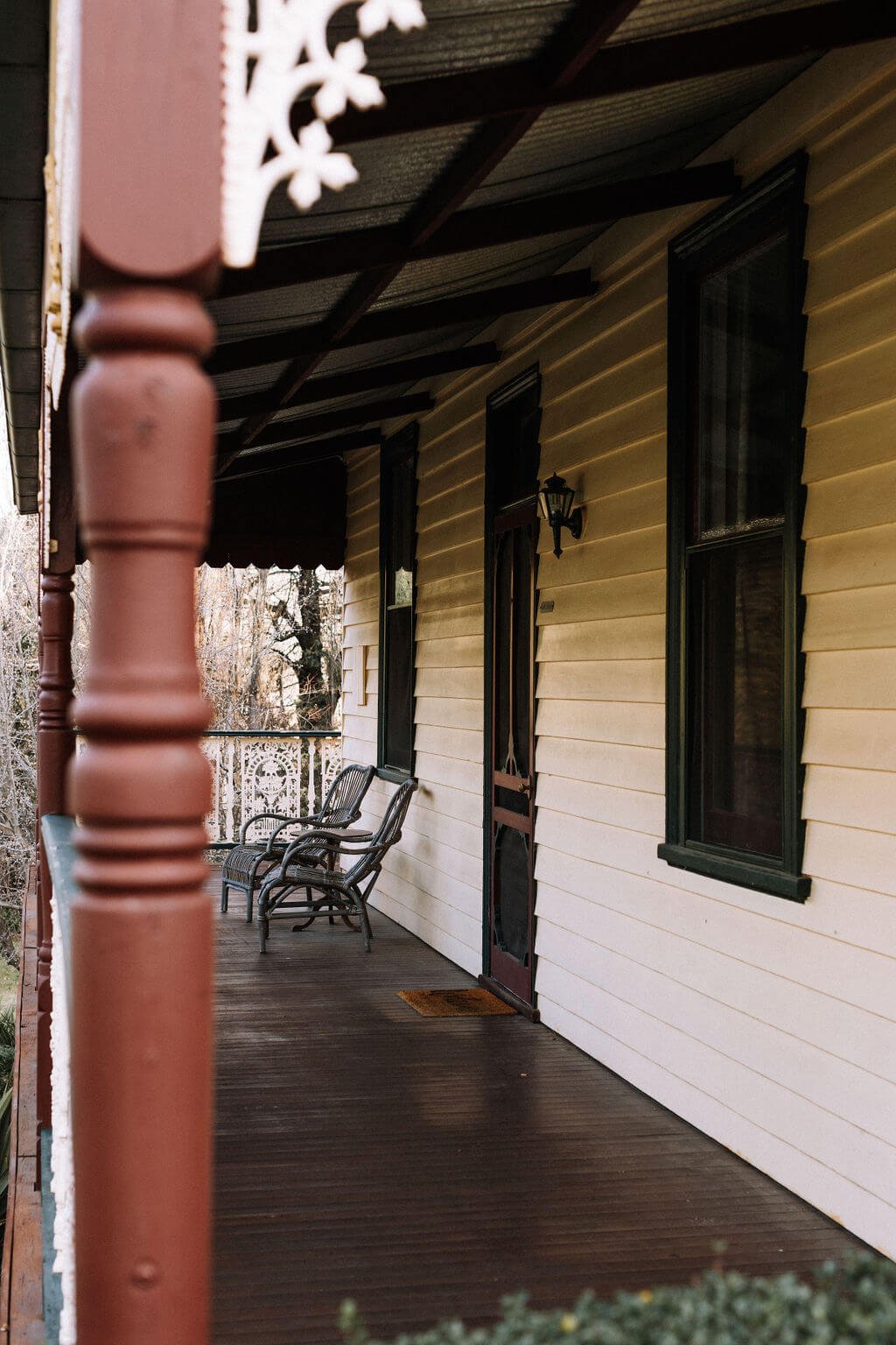 The Inn Beechworth, Luxury Accommodation - Kelly House. Traditional wooden porch with chairs and decorative post, featuring a wooden door, windows, and railing.
