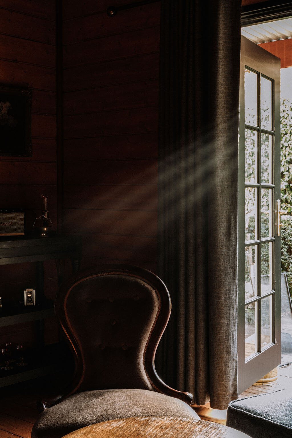 The Inn Beechworth, Luxury Accommodation - Kelly House. Cozy interior with vintage armchair, side table, and open French doors letting in natural light.
