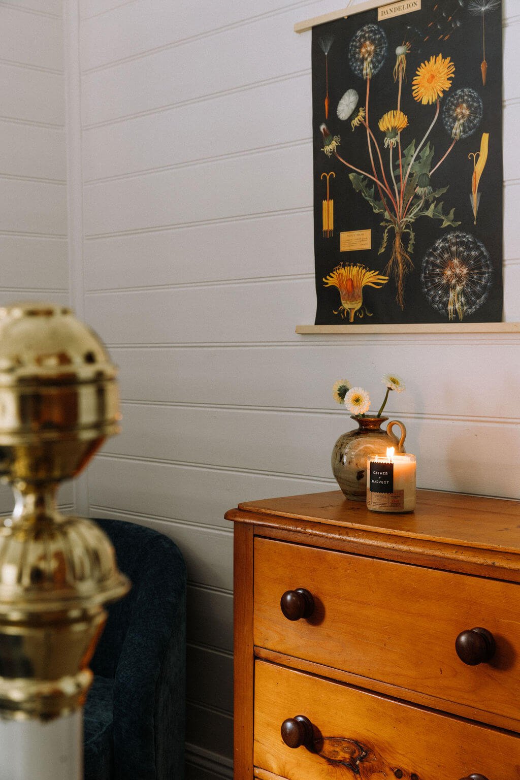 The Inn Beechworth, Luxury Accommodation - Kelly House. Cozy room with wooden dresser, decorative poster of dandelions, small vase with white flowers, and a lit candle.