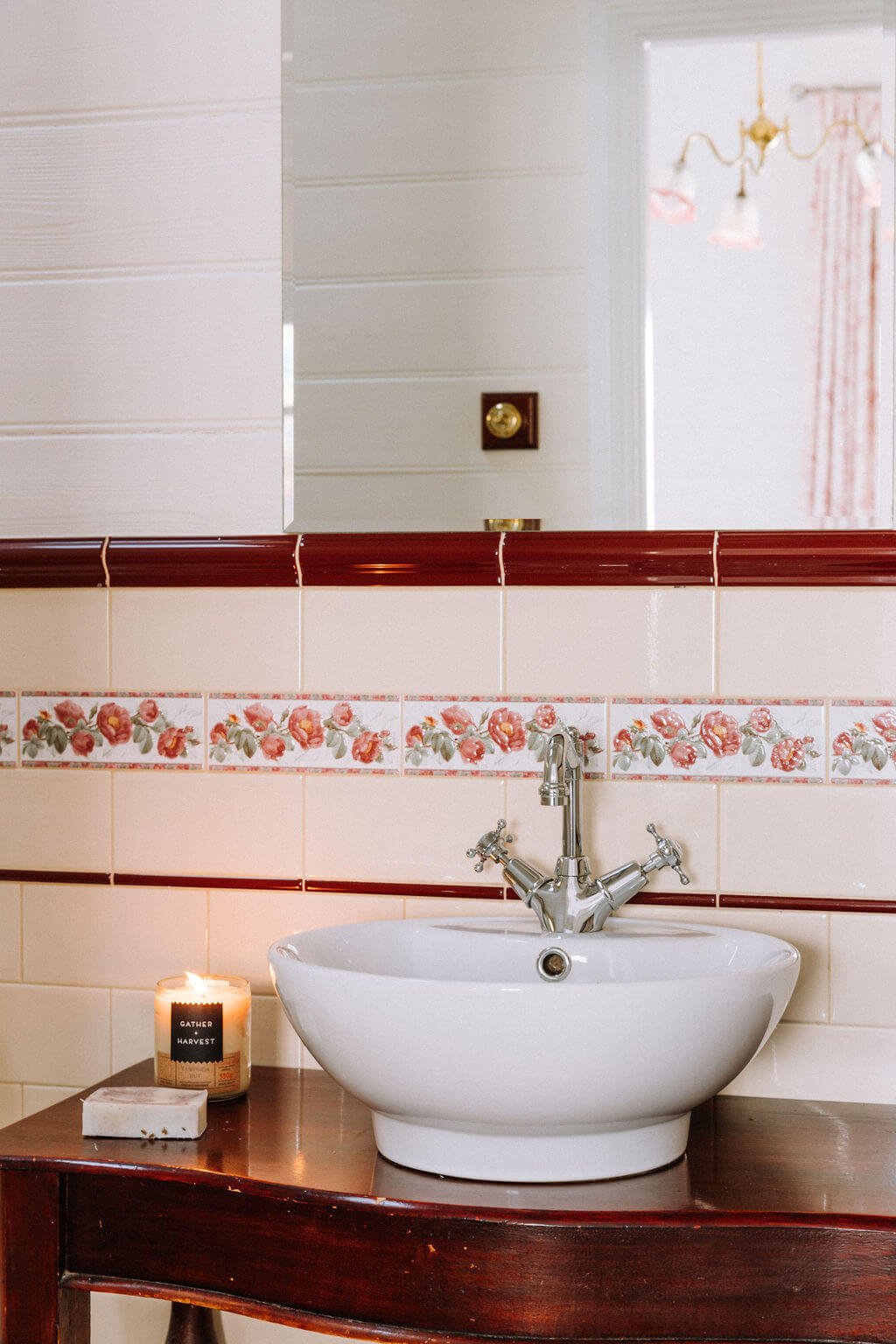 The Inn Beechworth, Luxury Accommodation - Kelly House. Bathroom sink with floral tiled backsplash, lit candle, and soap on a dark wooden counter.
