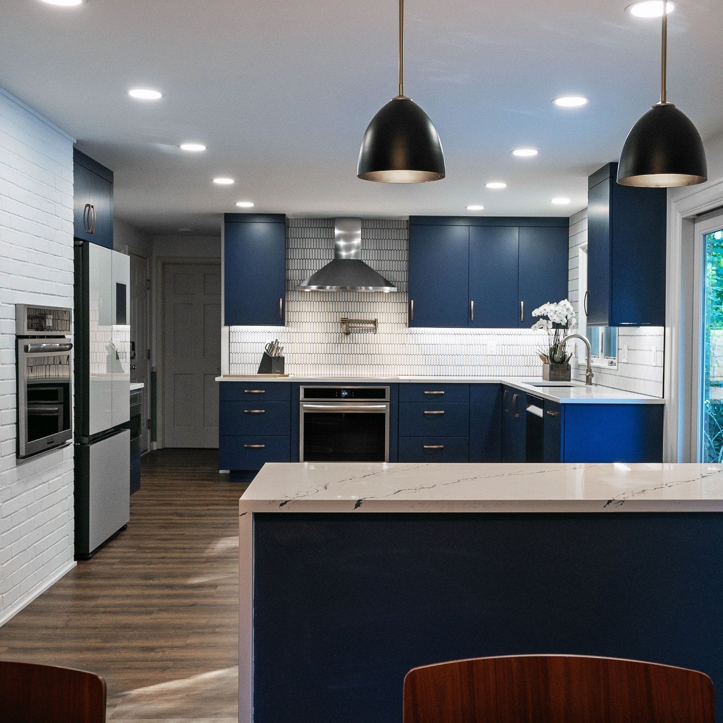 Just one more peek, because we know you love it as much as we do! Dive into the elegance of this kitchen, where the bold blue cabinets and chic black pendant lights strike the perfect balance with the minimalist white tiles. This space is more than j