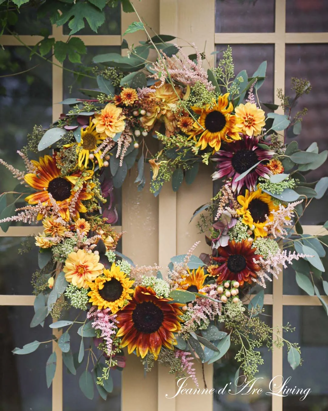 En efterårskrans med solsikker, asters, eucalyptusblade og små blomster, ophængt på en dør med et gitter.