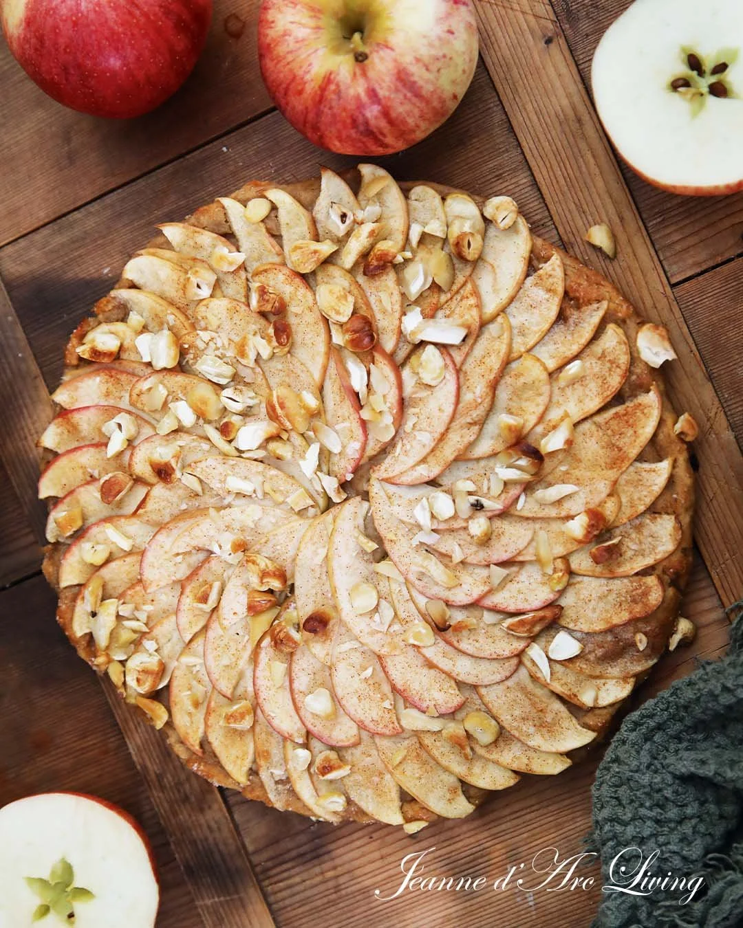 Rødt æble-crostata med skiver af æble og hakkede nødder på en træplade.