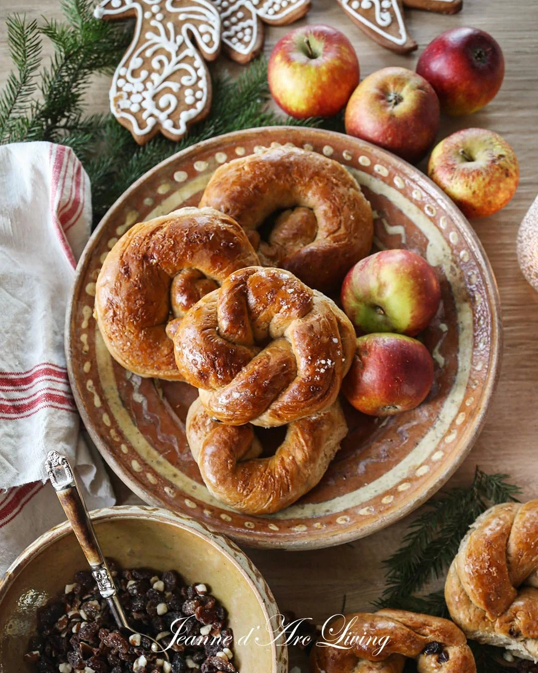 Morgenmad med små wienerbrød, æbler, en skål med mørke rosiner, og pynt af granatæbler og krydderurter.