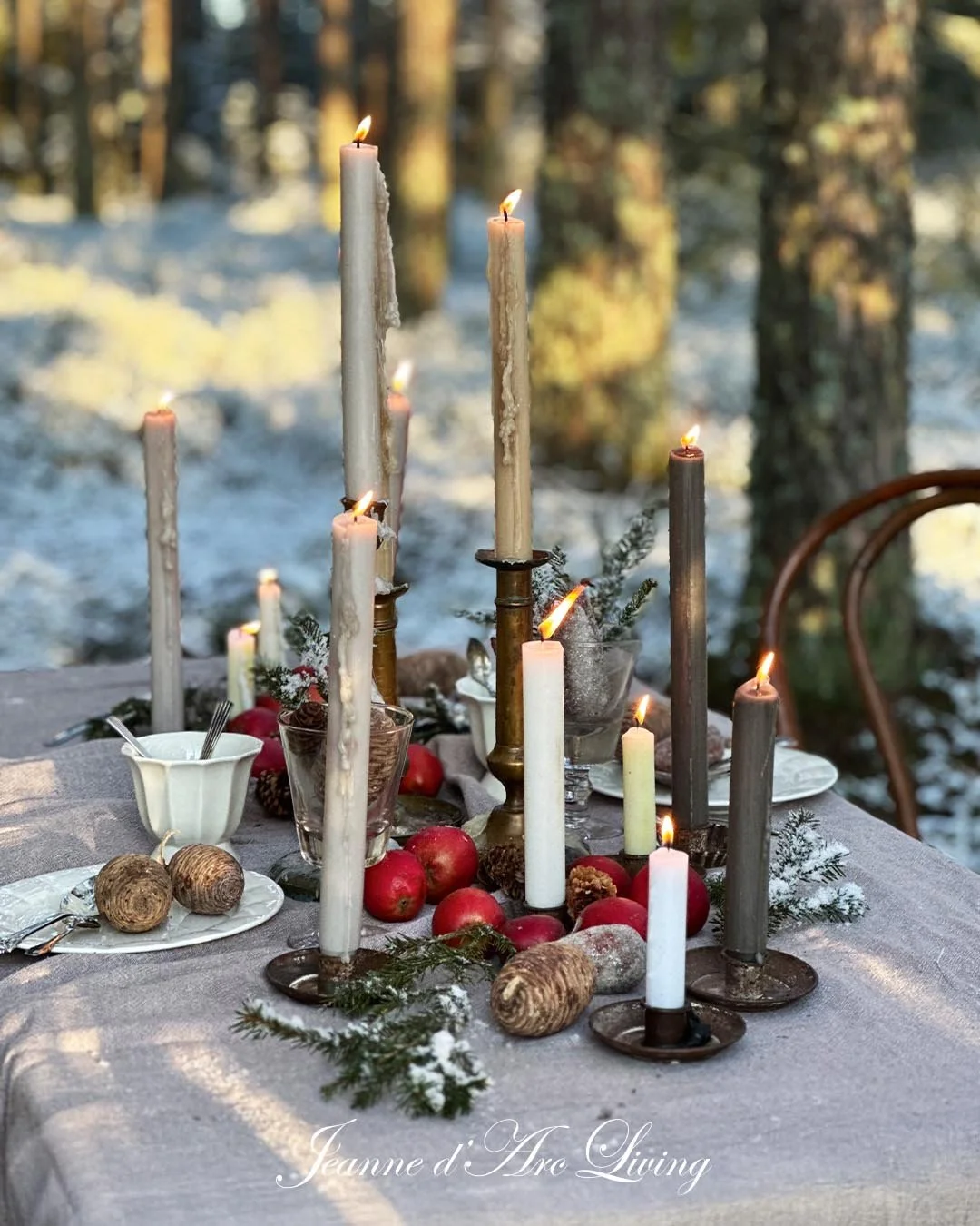 Udendørs spisebord dekoreret til jul med stearinlys, granræbter, æbler, kvæder og julekugler i en vinterskov.