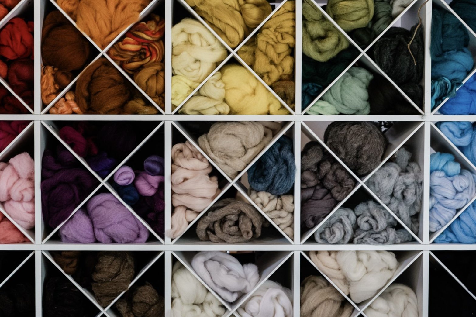 Colorful skeins of yarn neatly organized in a white shelf with individual compartments.