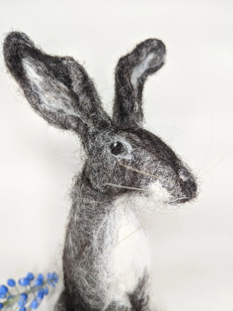 Felted wool sculpture of a rabbit with tall ears, set against a plain background.