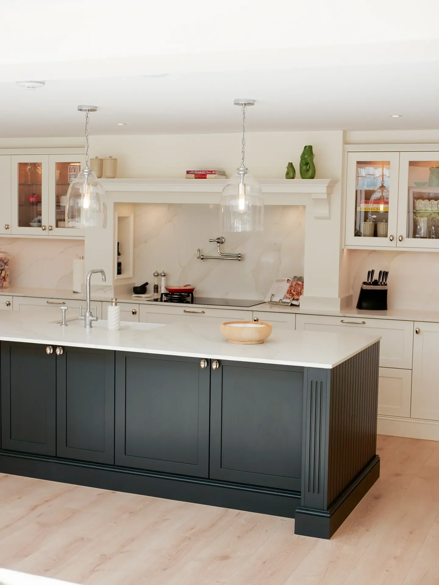 Modern kitchen with white upper cabinets, black lower island, marble countertops, pendant lighting, and decorative items.