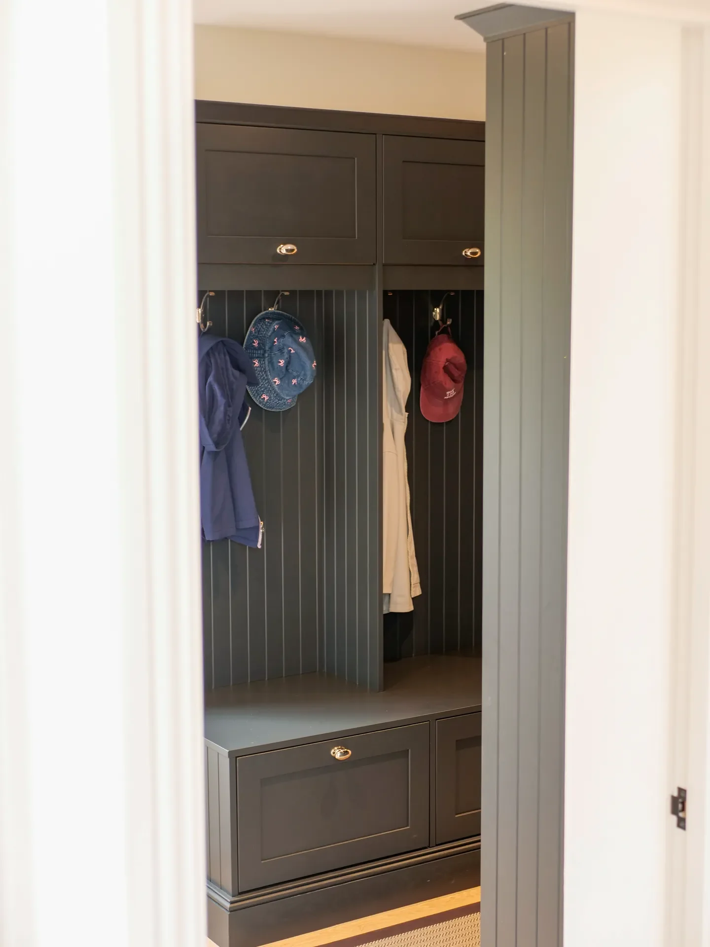 A gray entryway bench and coat closet with hooks holding jackets and hats, framed by a doorway.