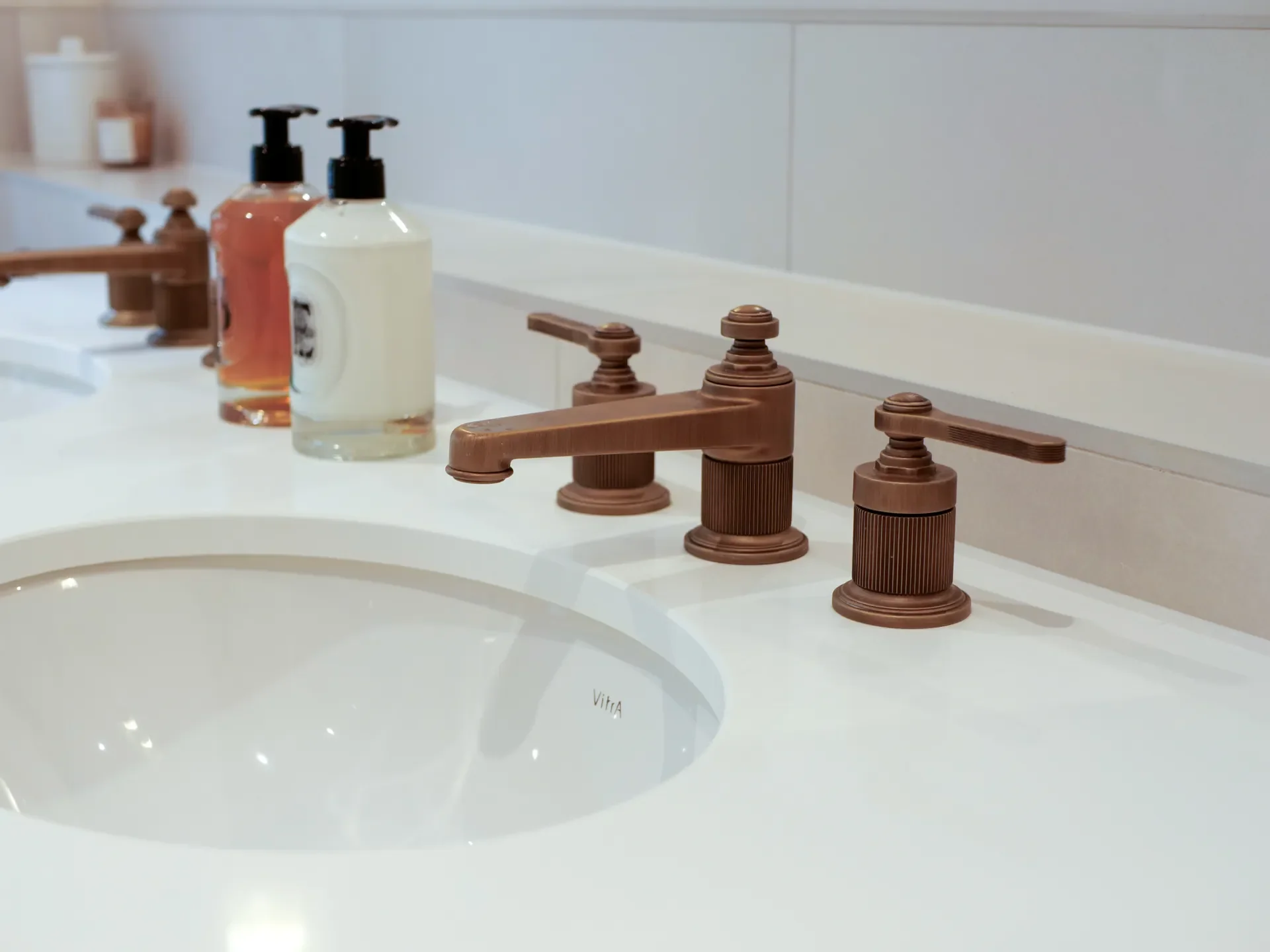 Bathroom sink with copper-colored faucet handles and a countertop with soap dispensers and bottles.
