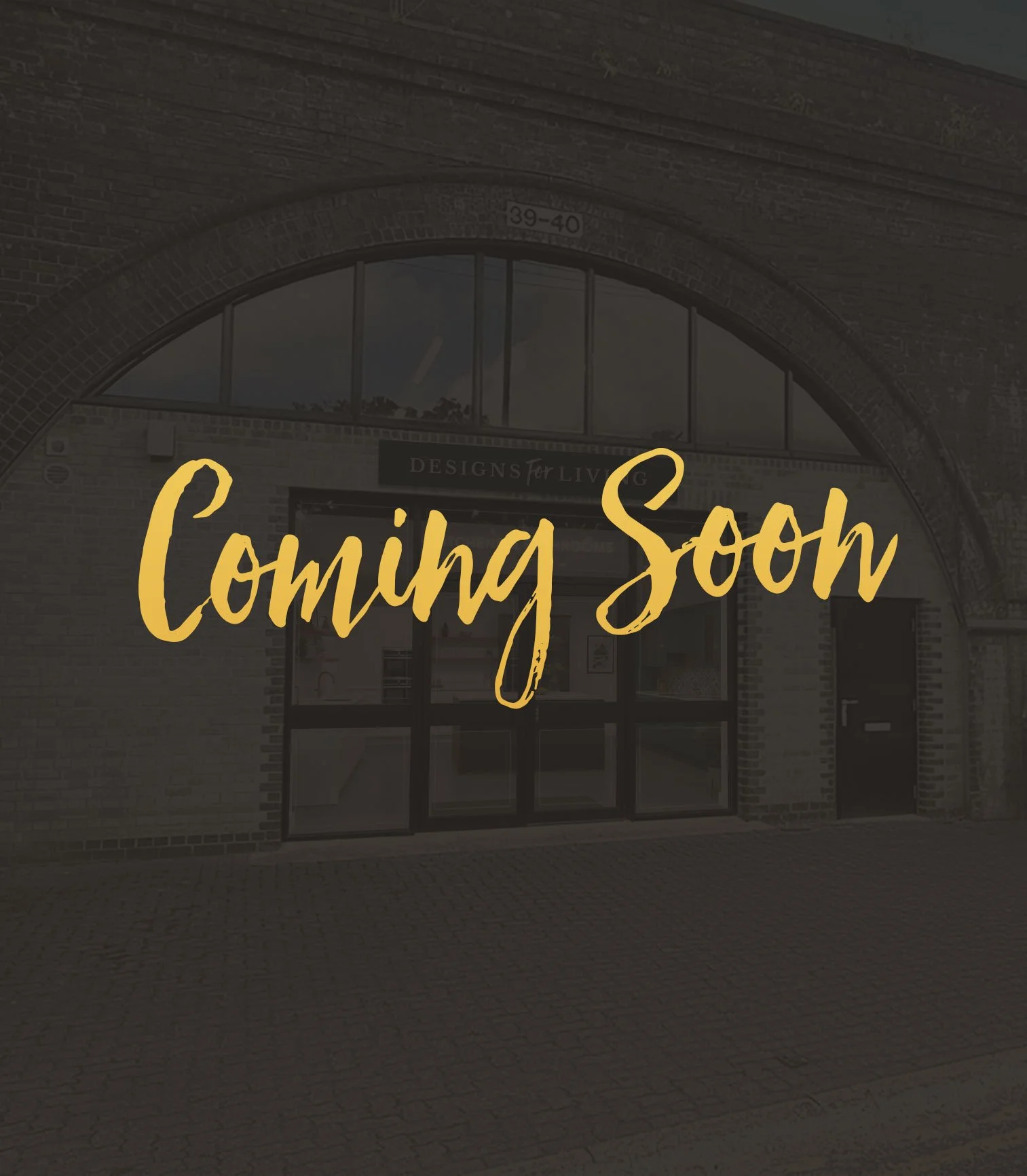 A storefront with a message overlay that says 'Coming Soon' in yellow script font, with a brick archway and glass entrance.