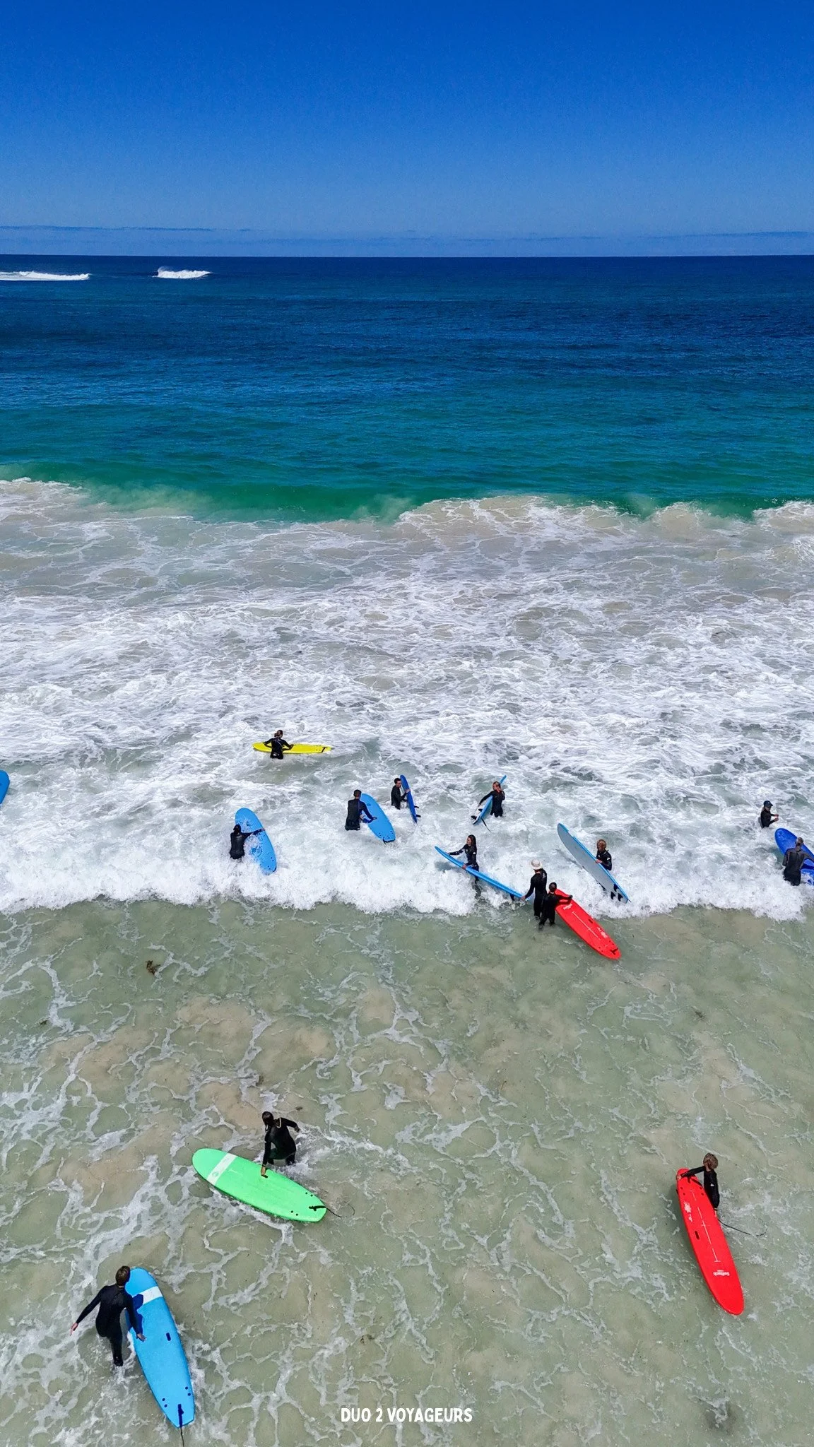 People learning to surf at the beach with colorful surfboards and clear ocean water.