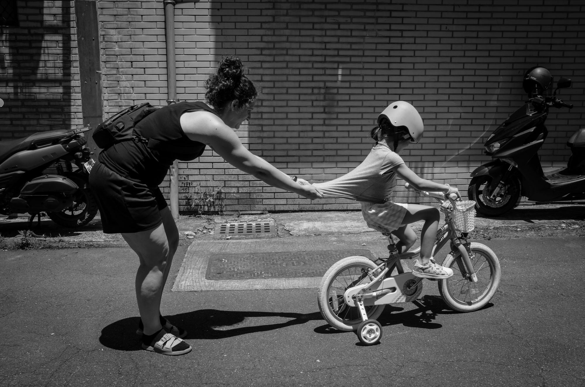A mother grabs onto the back of her young daughter's shirt as she tries to ride away on her bike in Taipei, Taiwan. 