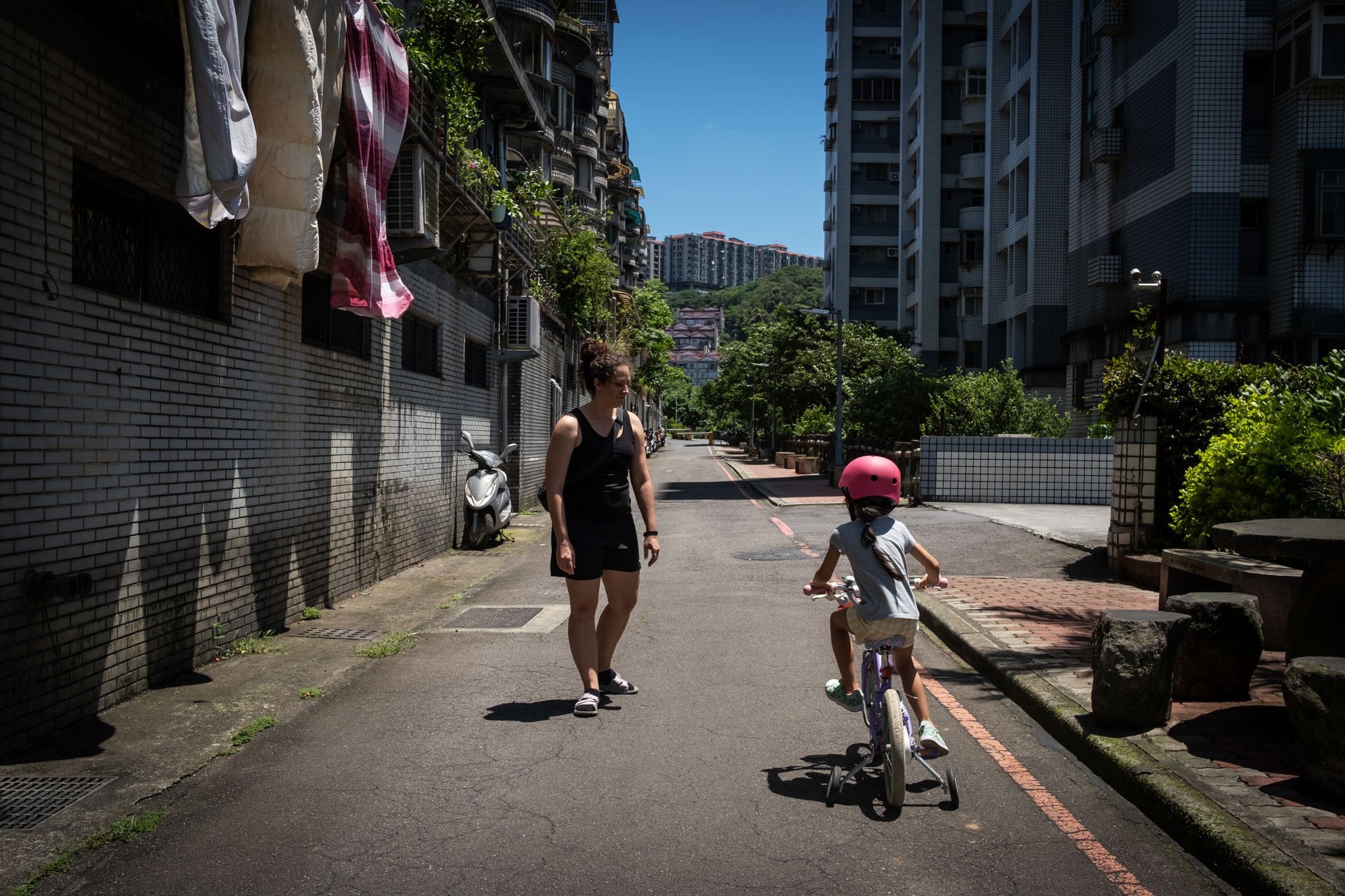 A mother accompanies her young daughter as she rides her bike on the lane outside their apartment in Taipei, Taiwan. 