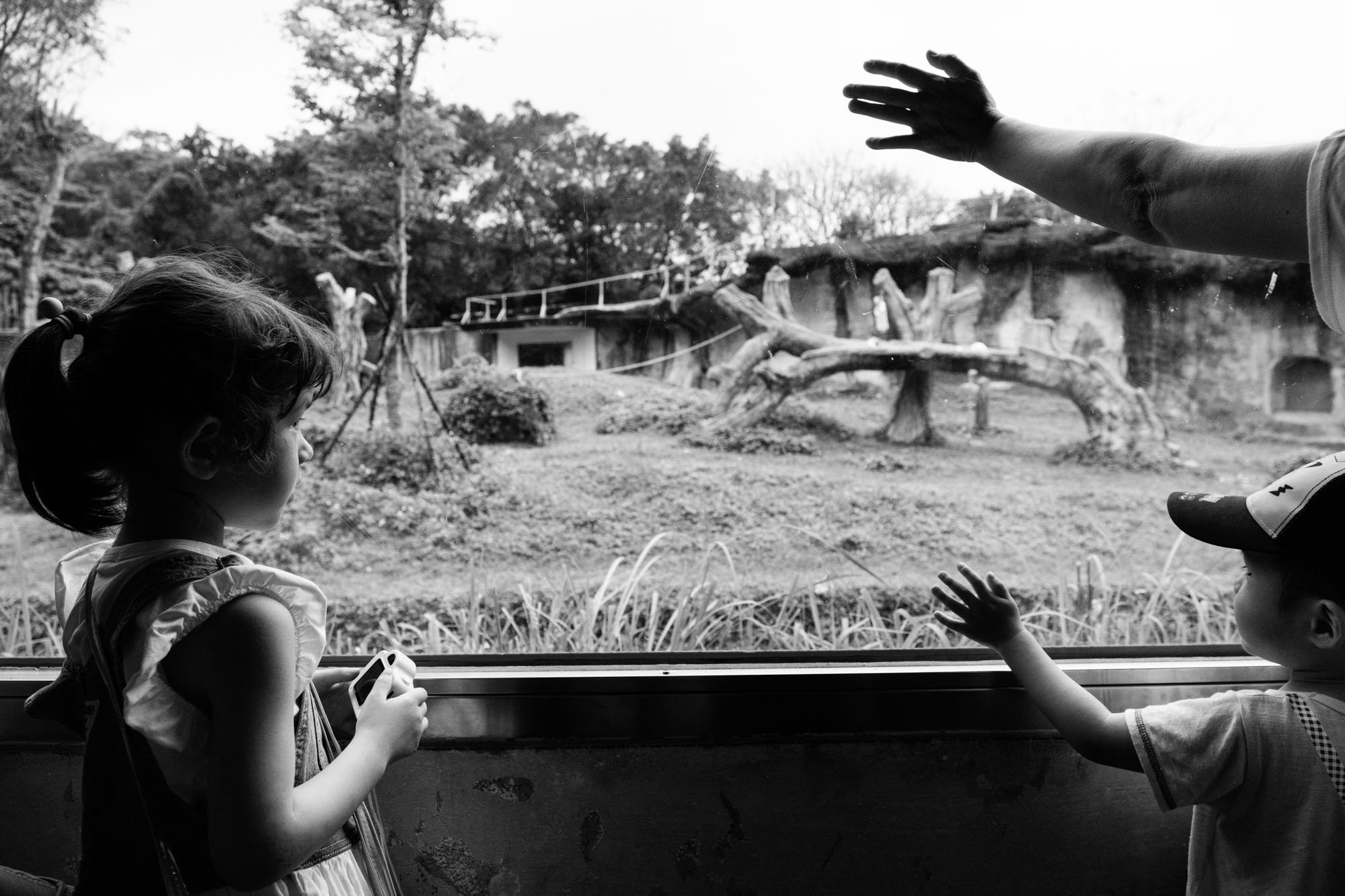 A little girl is looking at other people standing next to her by the chimpanzee display at the Taipei Zoo. 