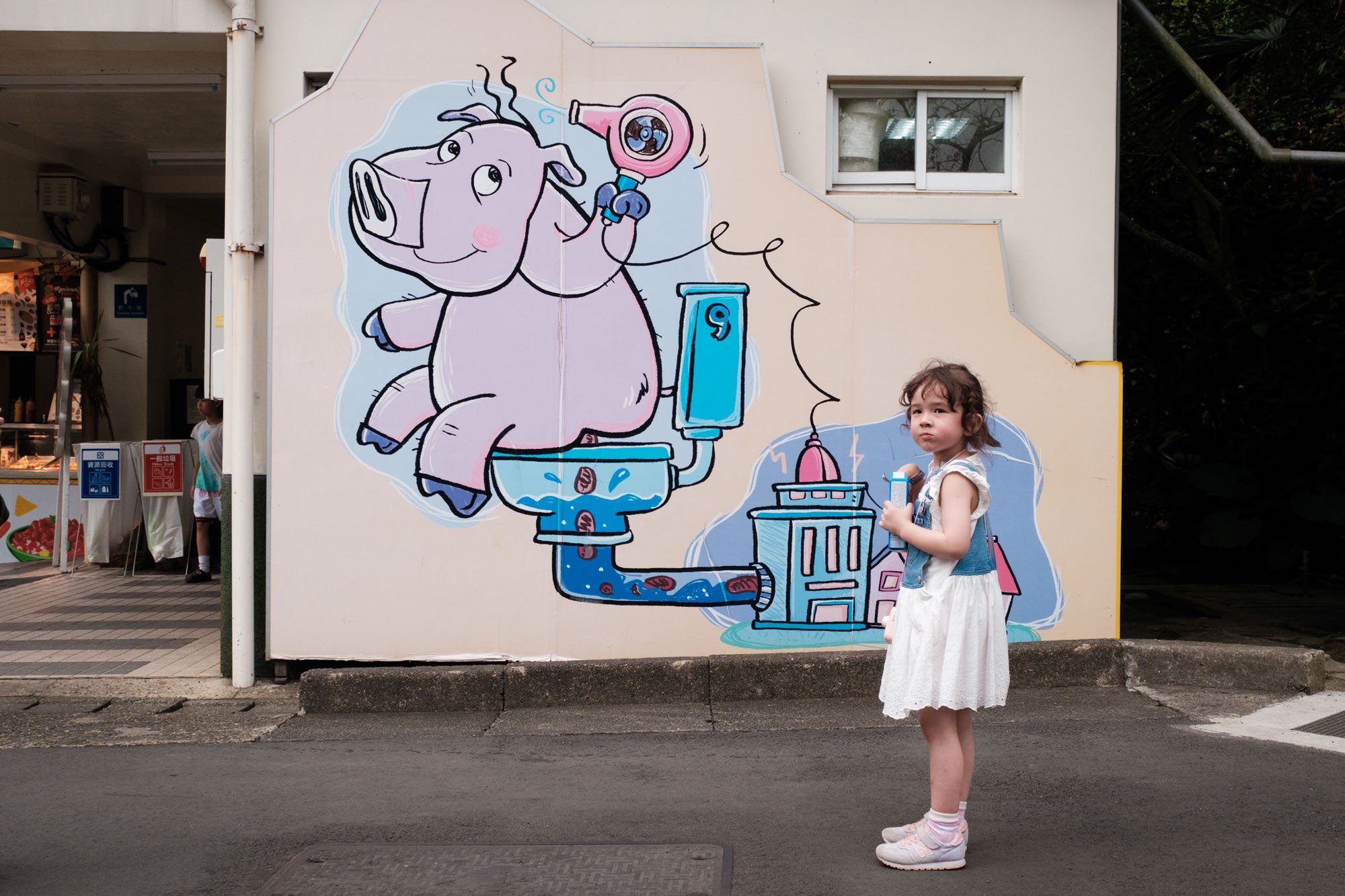 A little girl stands next to a painting of a hippo pooping on a toilet on the outside wall of a bathroom at the Taipei Zoo.
