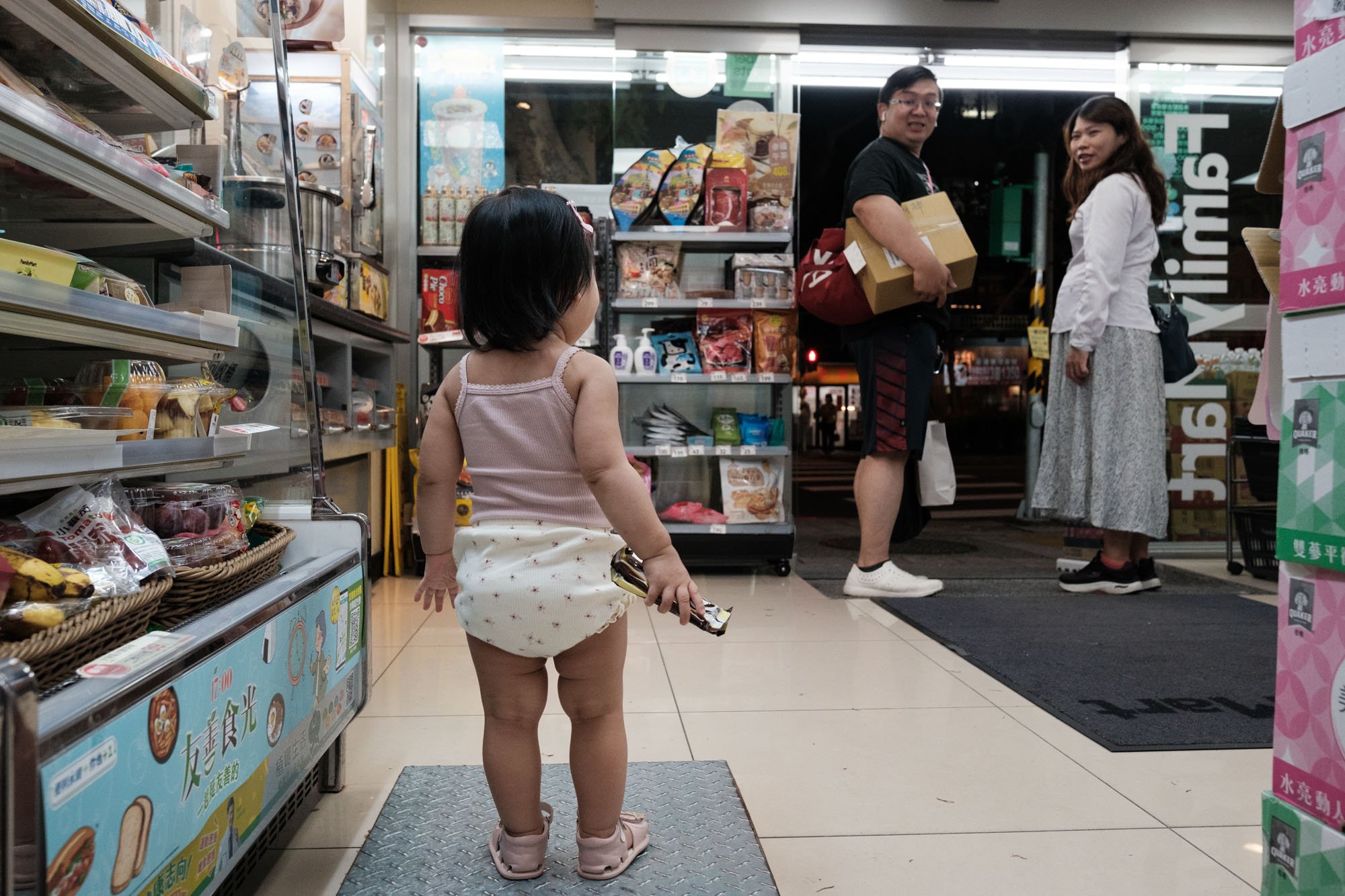A little girl looks at a couple leaving Family Mart during a family photography session in Taipei, Taiwan.
