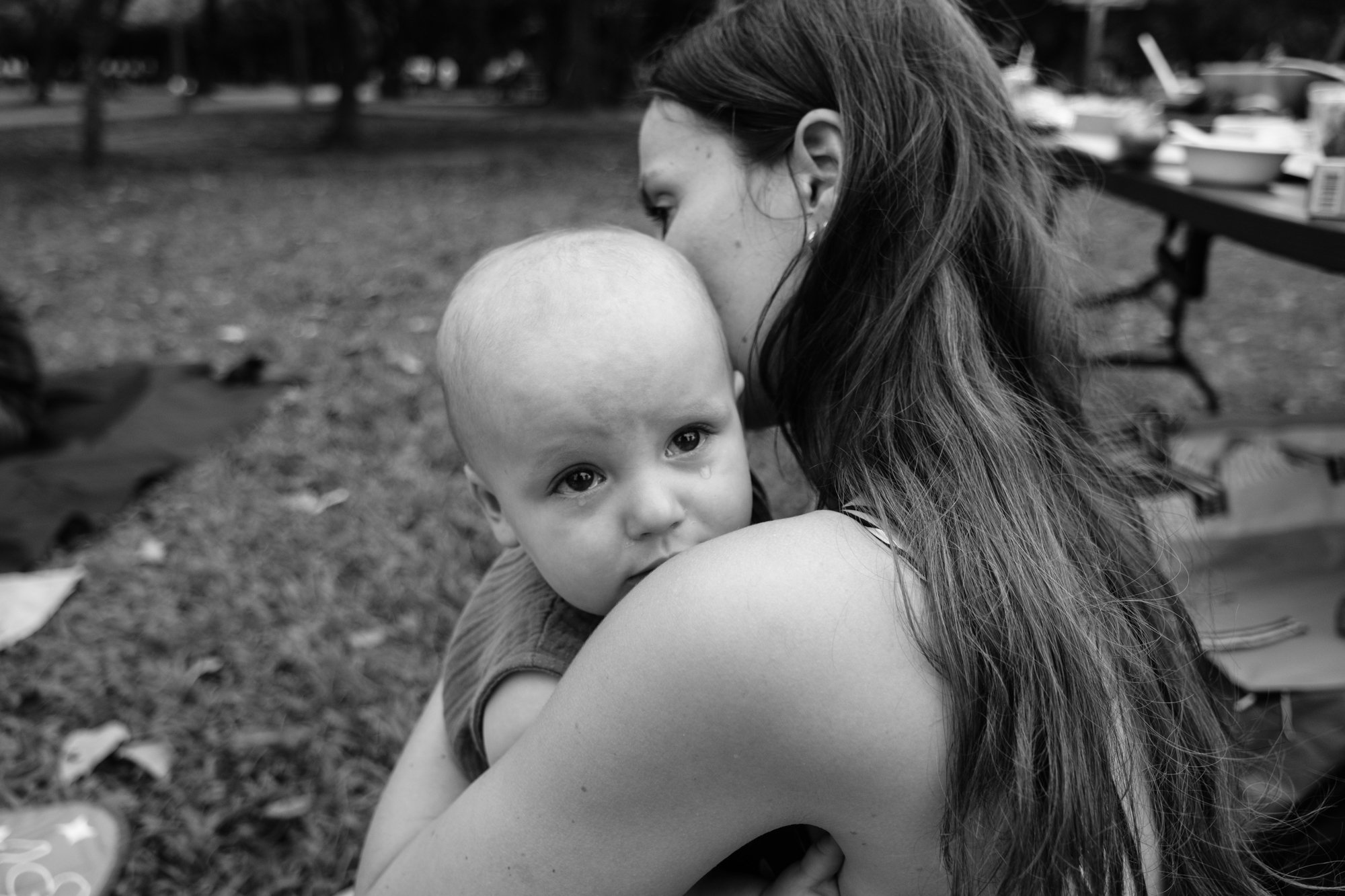 A woman comforts her baby son as two big tears fall from his eyes. Photographed during a birthday party by Taipei family photographer Cahleen Hudson.