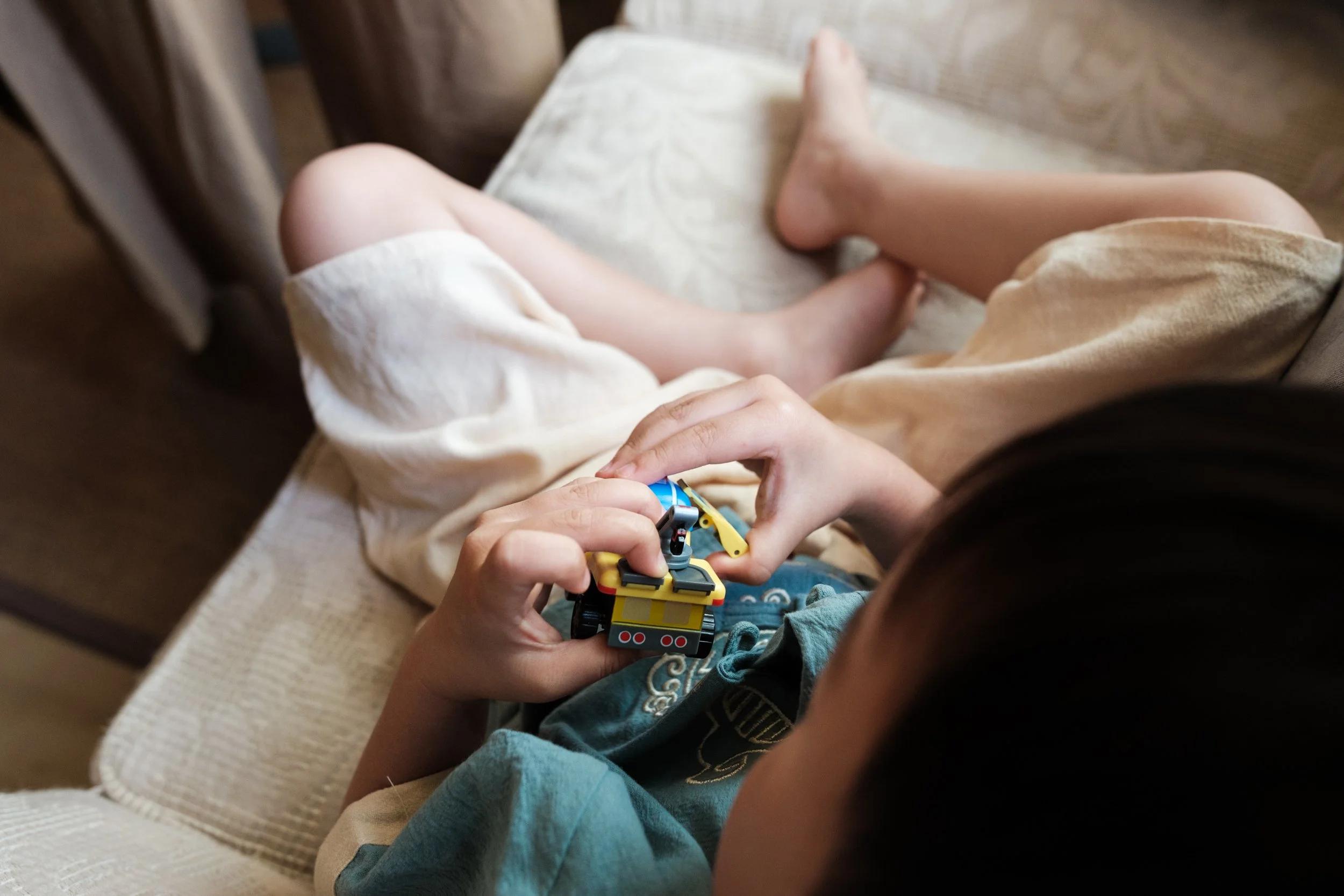 A close-up photo of a little boy's hands holding a toy truck as he sits on a sofa. Photographed by family photographer Cahleen Hudson in Taipei during a family photoshoot at home.
