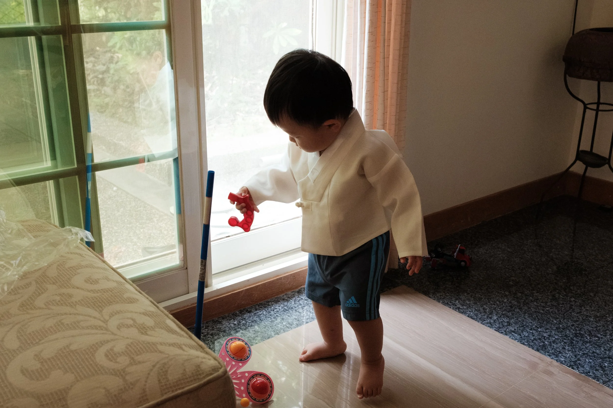 A toddler boy playing with a toy in front of a sliding glass door with light streaming through it. Photographed by Taipei family photographer Cahleen Hudson during a home session on Yangmingshan.
