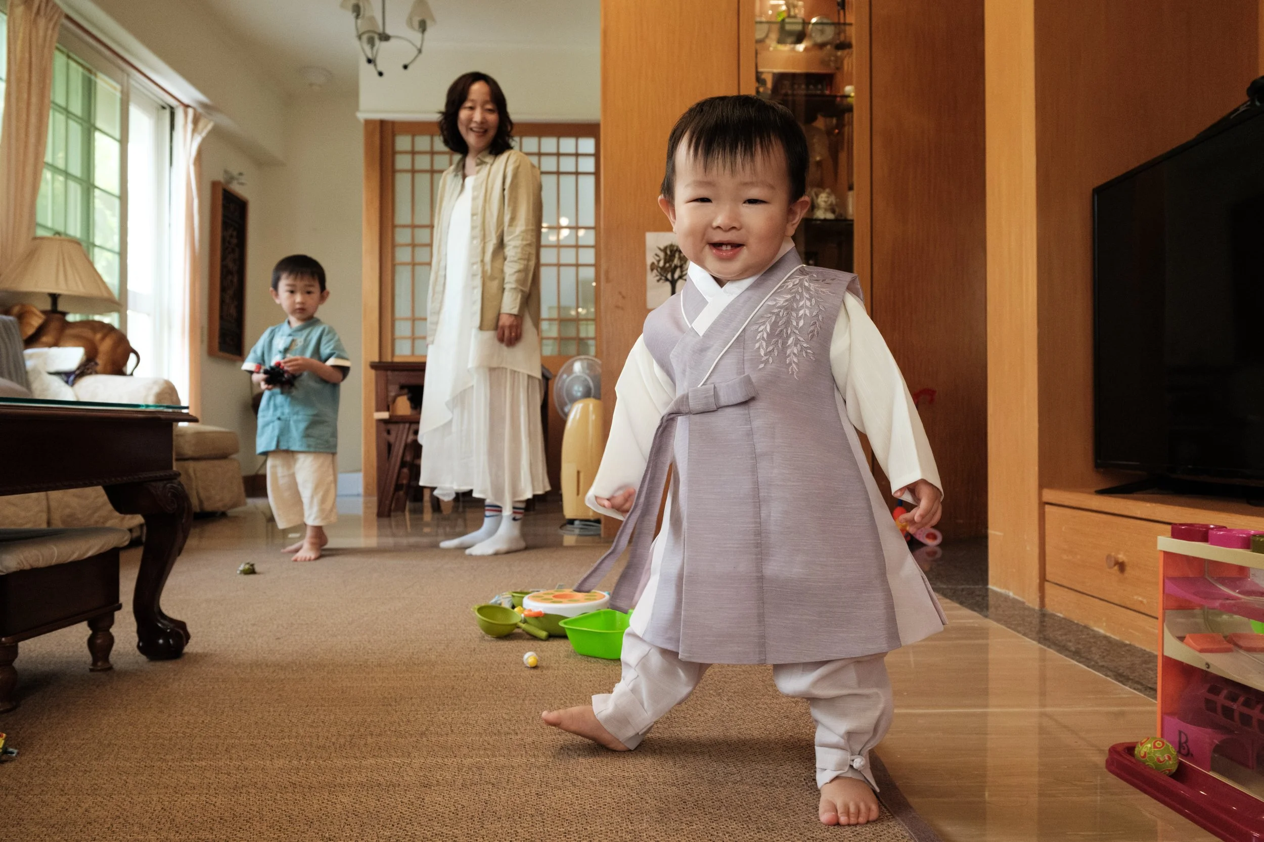 A toddler is wearing a traditional Korean hanbok and his mother and older brother are in the background. Photographed by family photographer Cahleen Hudson in Taipei.
