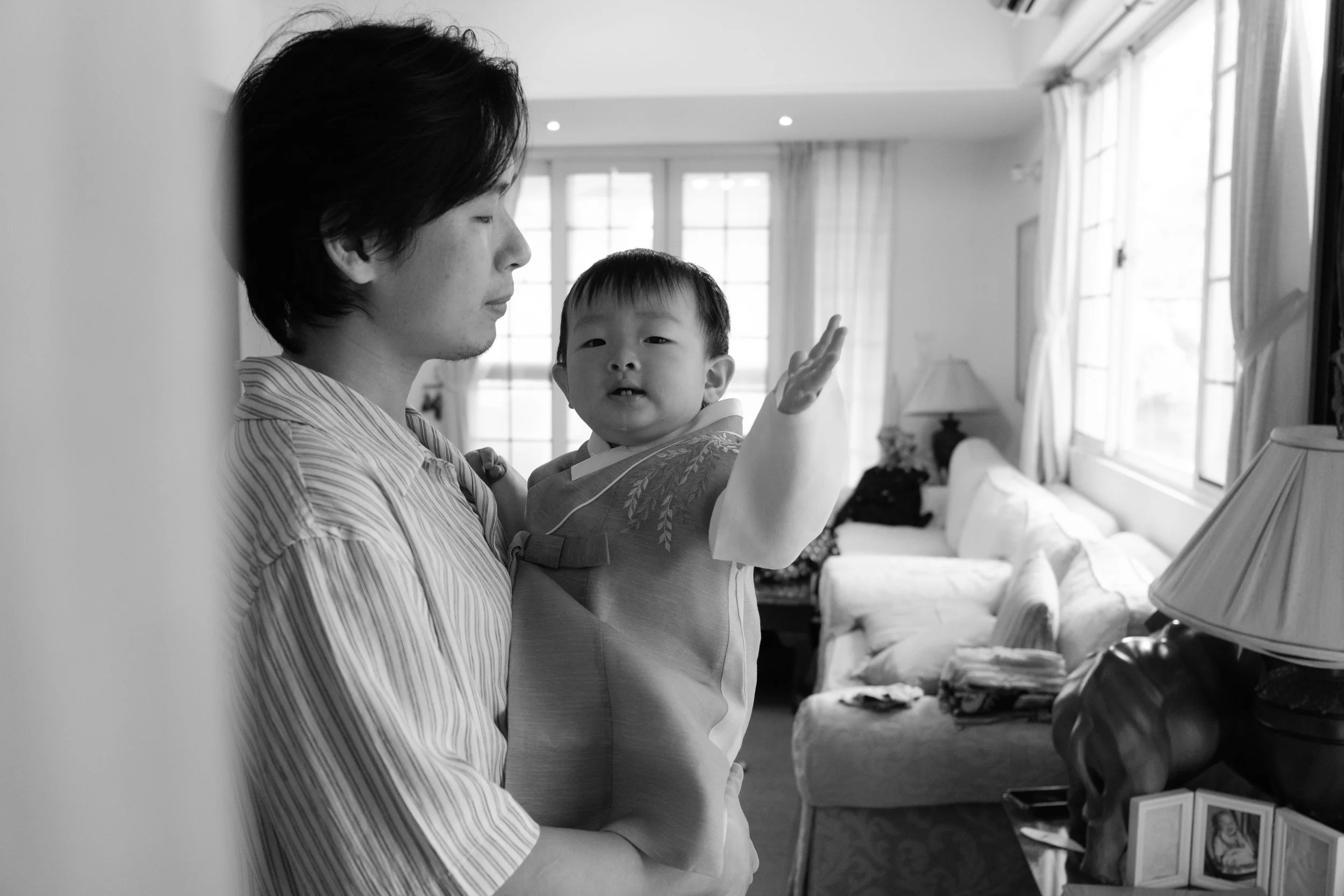 A black and white photo of a father holding their toddler son, who is wearing a Korean hanbok. Captured during a home family photoshoot in Taipei.