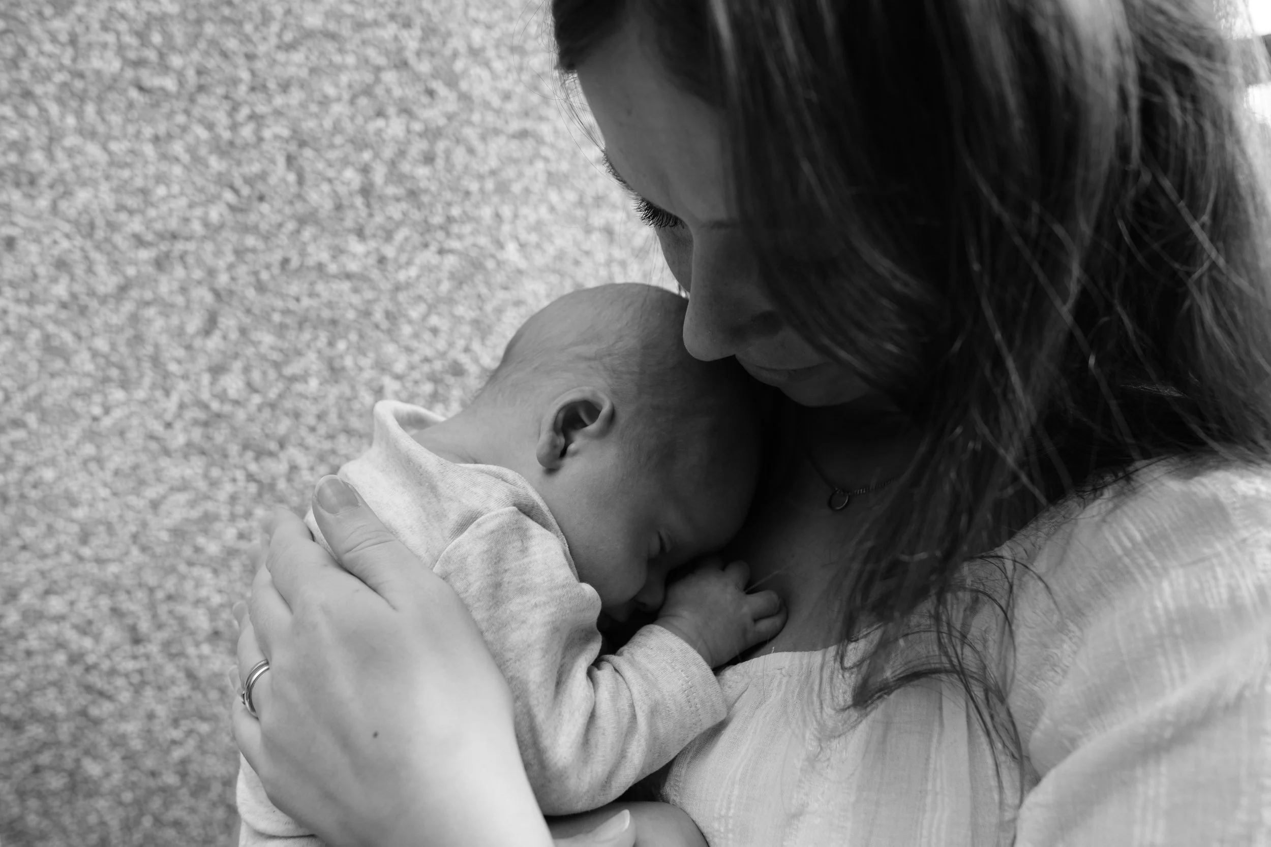 A black and white image of a young mother holding her newborn baby boy on a balcony in Taipei. The baby is nestled under her chin.