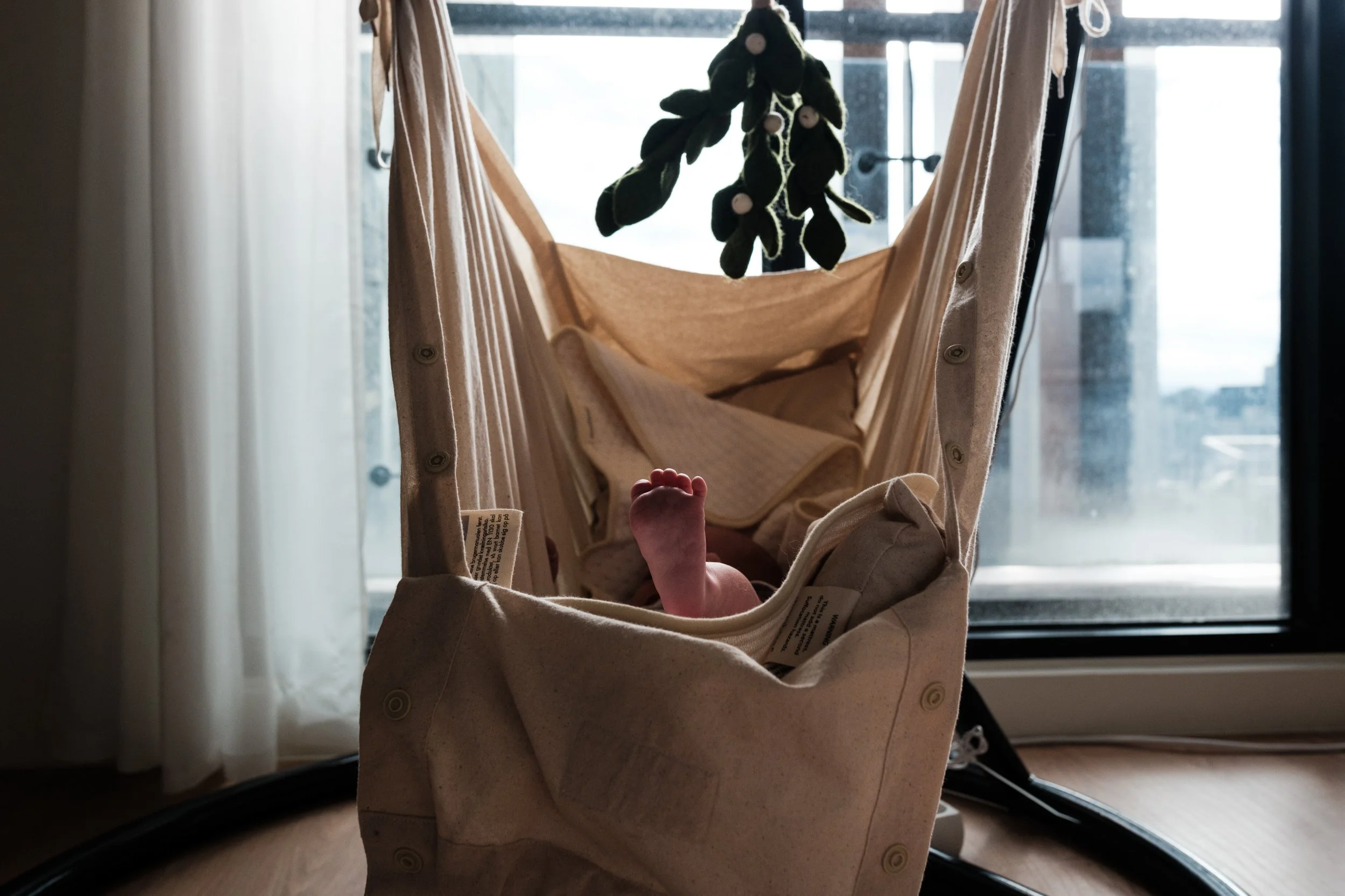 A color image of a newborn baby's foot poking out over the top of his baby swing. Golden light is shining on the little foot.