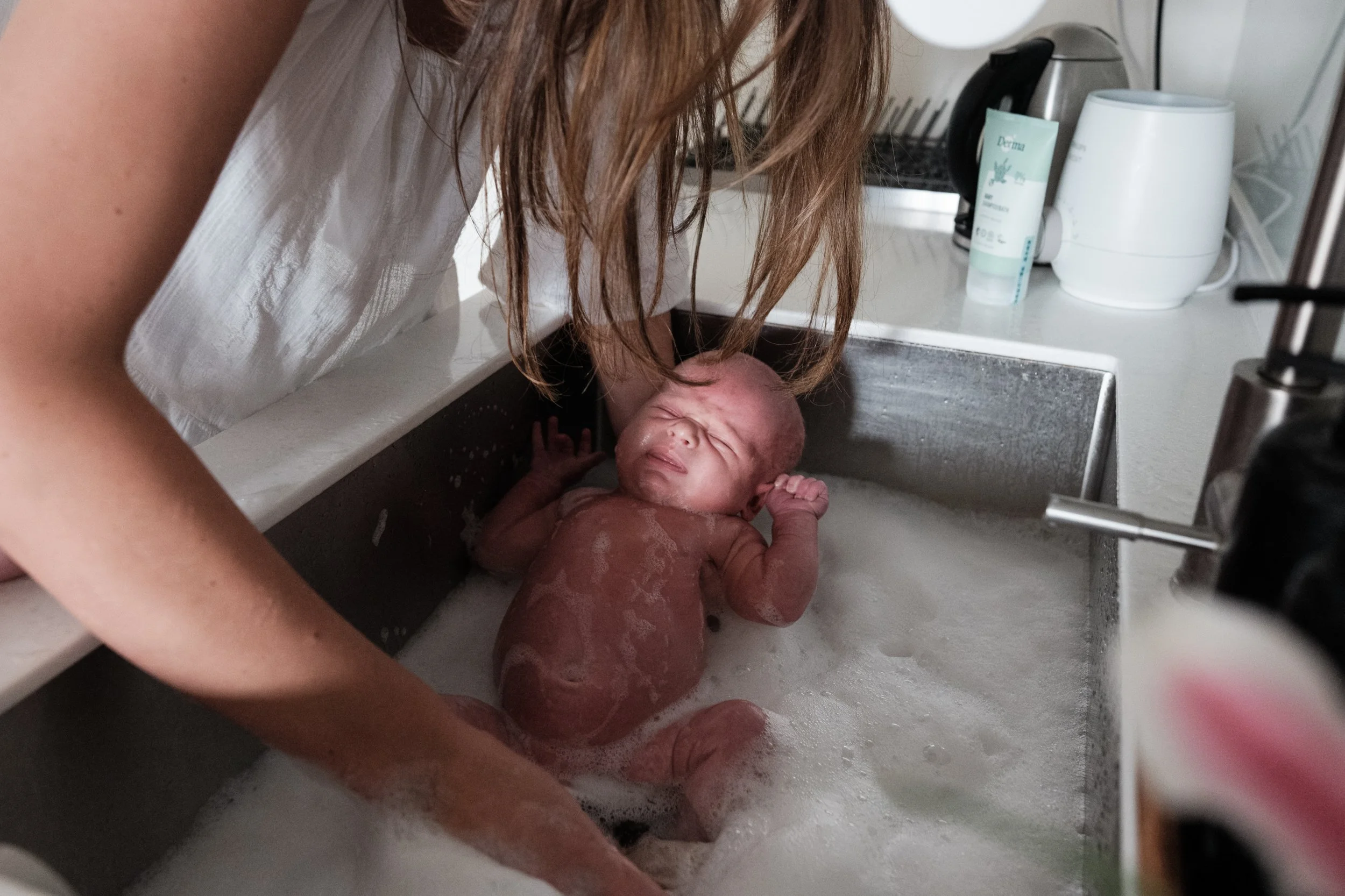 A mother is bathing her newborn baby boy in a sink in an apartment in Taipei. Photographed by newborn photographer Cahleen Hudson.