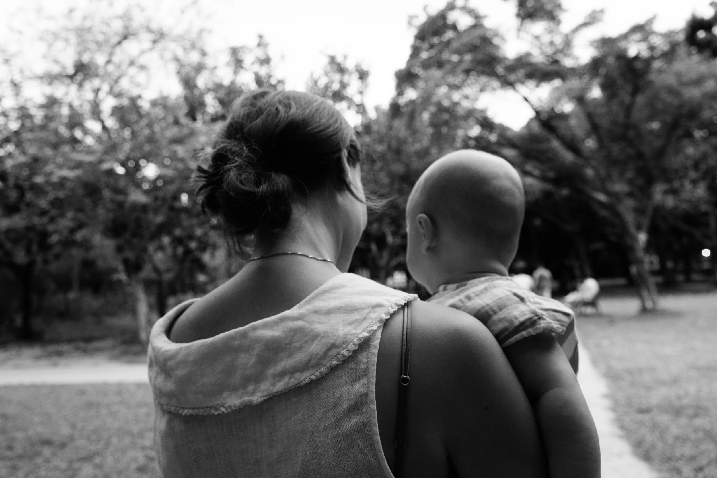 A black and white image of the back of a mother and baby as they walk down a lane in Daan Park in Taipei. Photographed by family photographer Cahleen Hudson.
