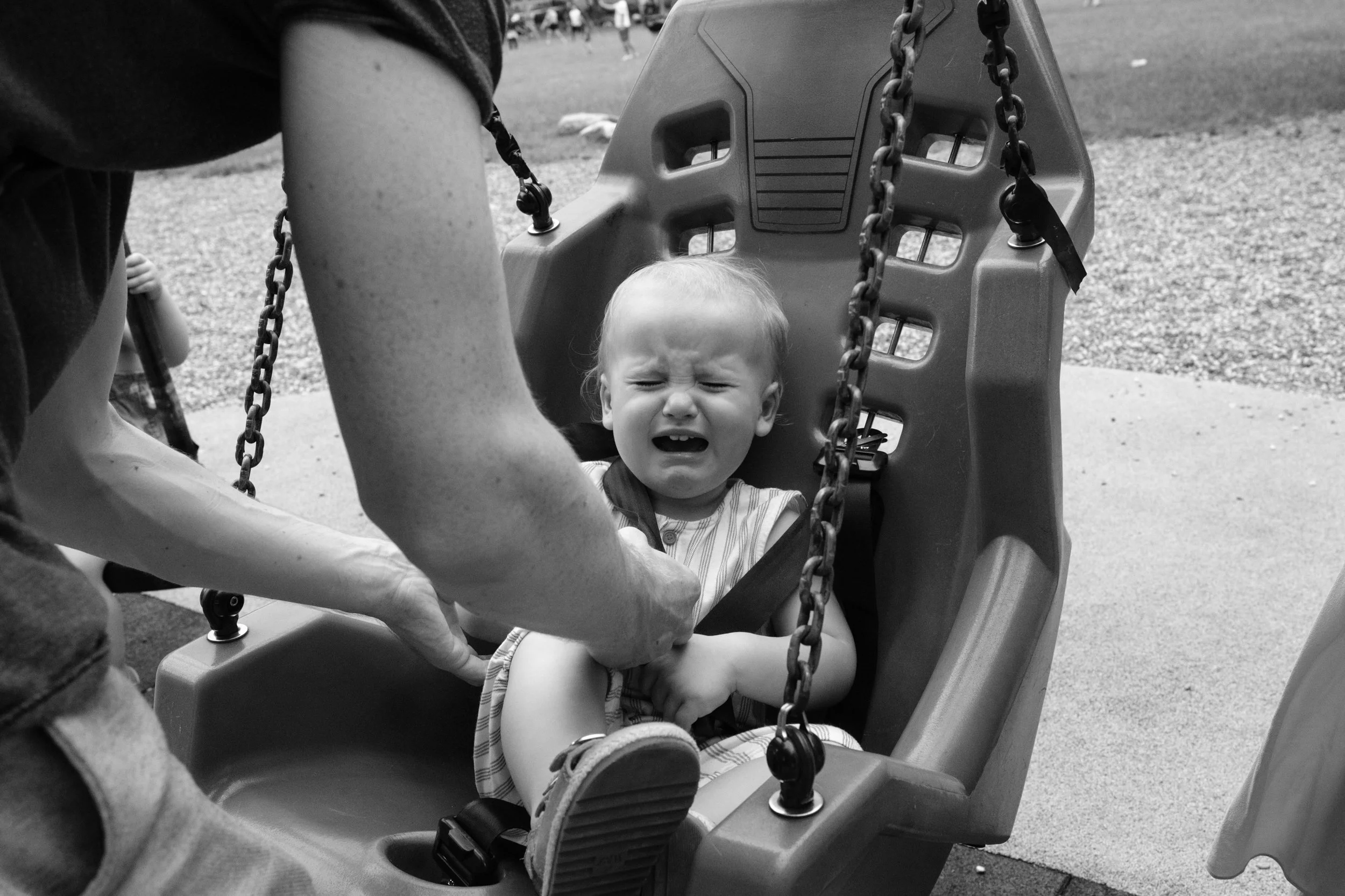 A black and white image of a toddler boy crying on a swing at a playground. Captured by Taipei documentary family photographer Cahleen Hudson.