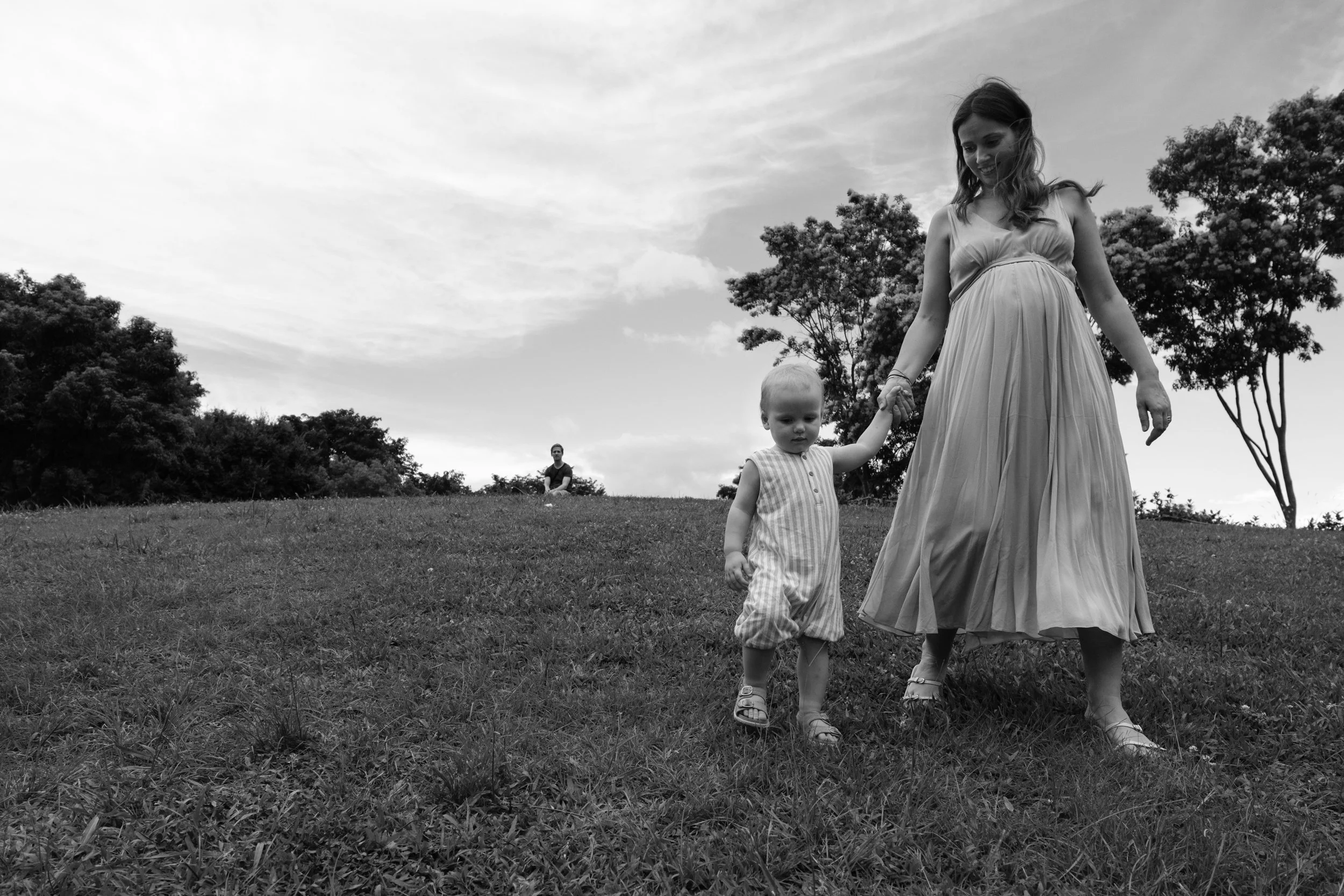 A black and white image of a mother holding her young son's hand on a grassy hill at Huashan Creative Park in Taipei. The father is in the background watching them.