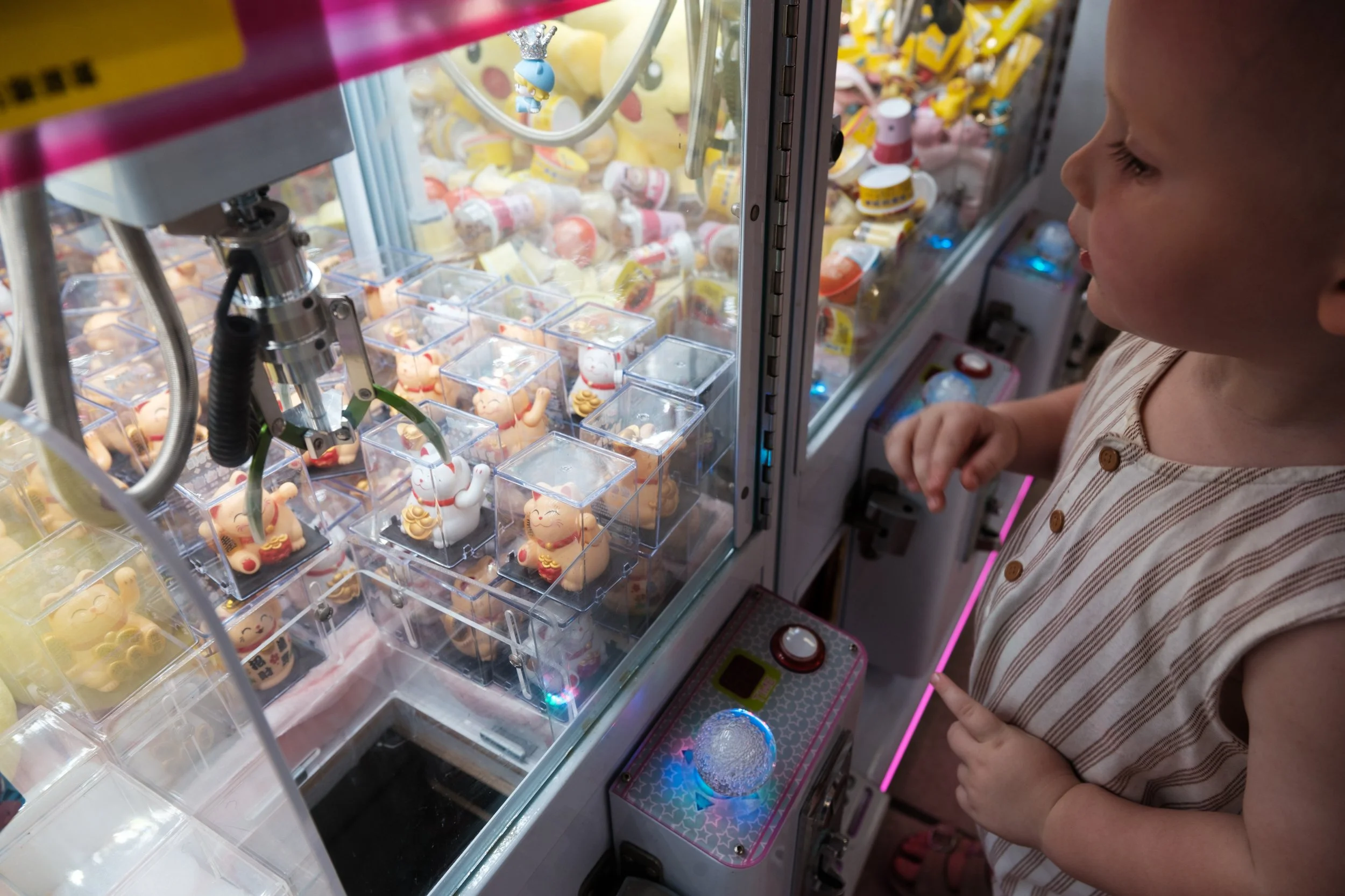 A little boy is playing with a claw machine. The light from the machine is illuminating his face. Photographed by Taipei family photographer Cahleen Hudson.