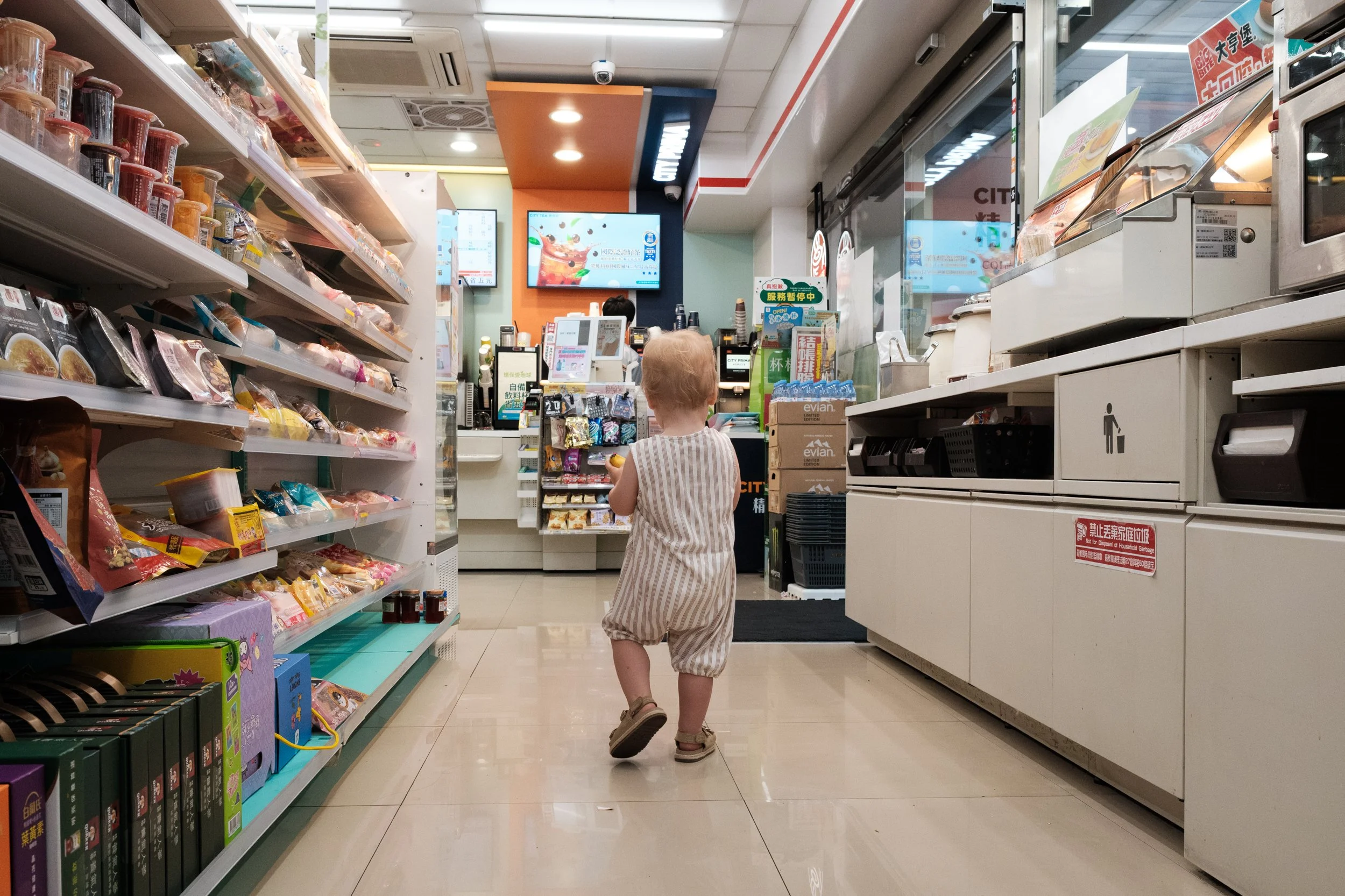 A color image of a toddler boy standing in an aisle in 7-Eleven in Taipei, Taiwan. The aisles are full of snacks.