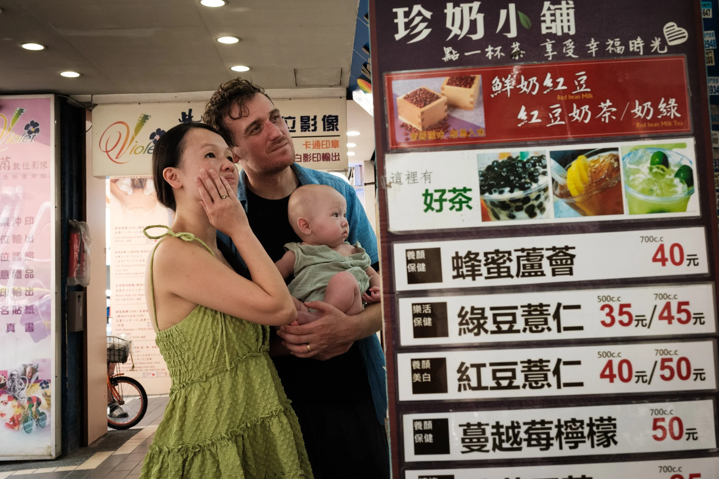  A couple and a baby are looking at a menu for a drink stand. Photographed by taipei family photographer Cahleen Hudson. 