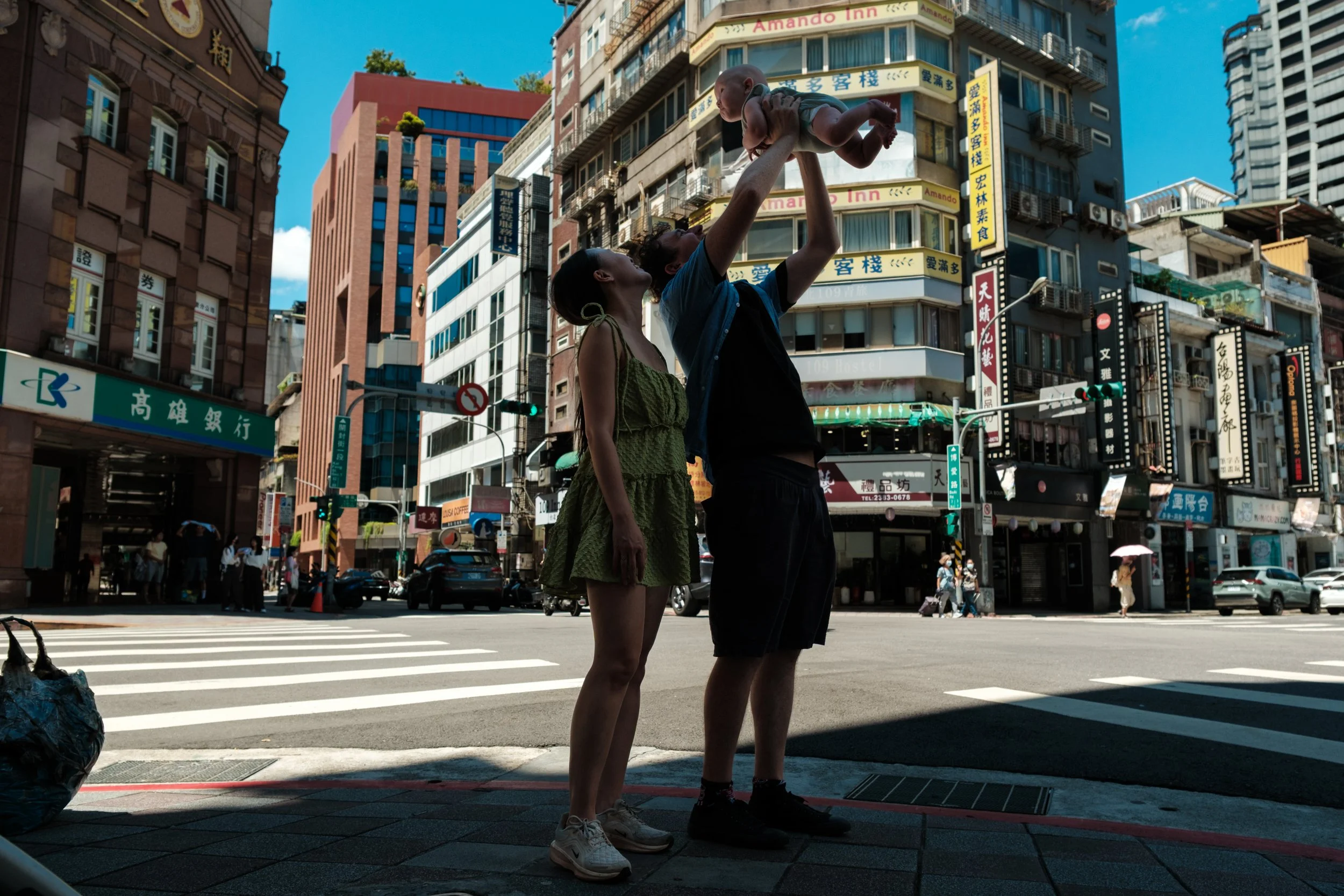 A color photo of a couple holding up their baby with a busy Taipei street behind them.