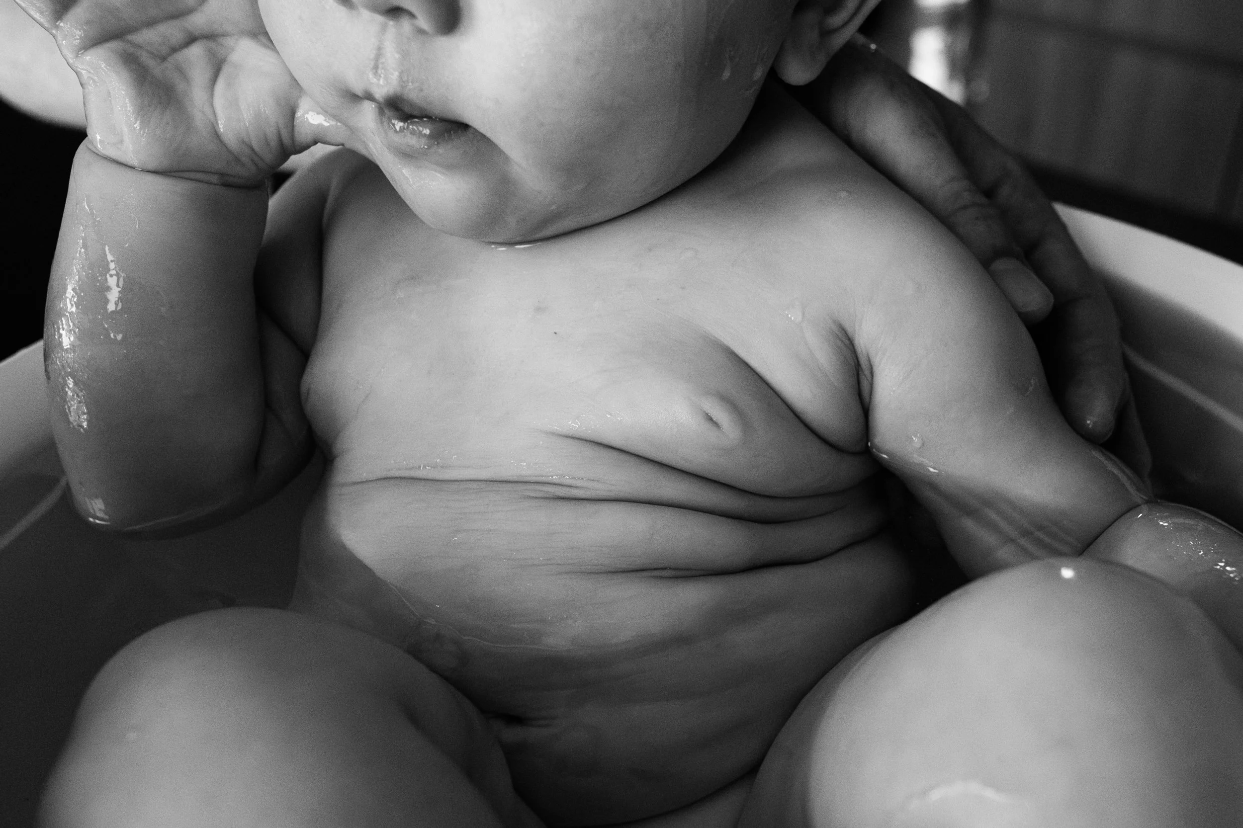 A close up black and white photo of a baby's fat rolls as he sits in a small bathtub. Captured by Taipei family photographer Cahleen Hudson.