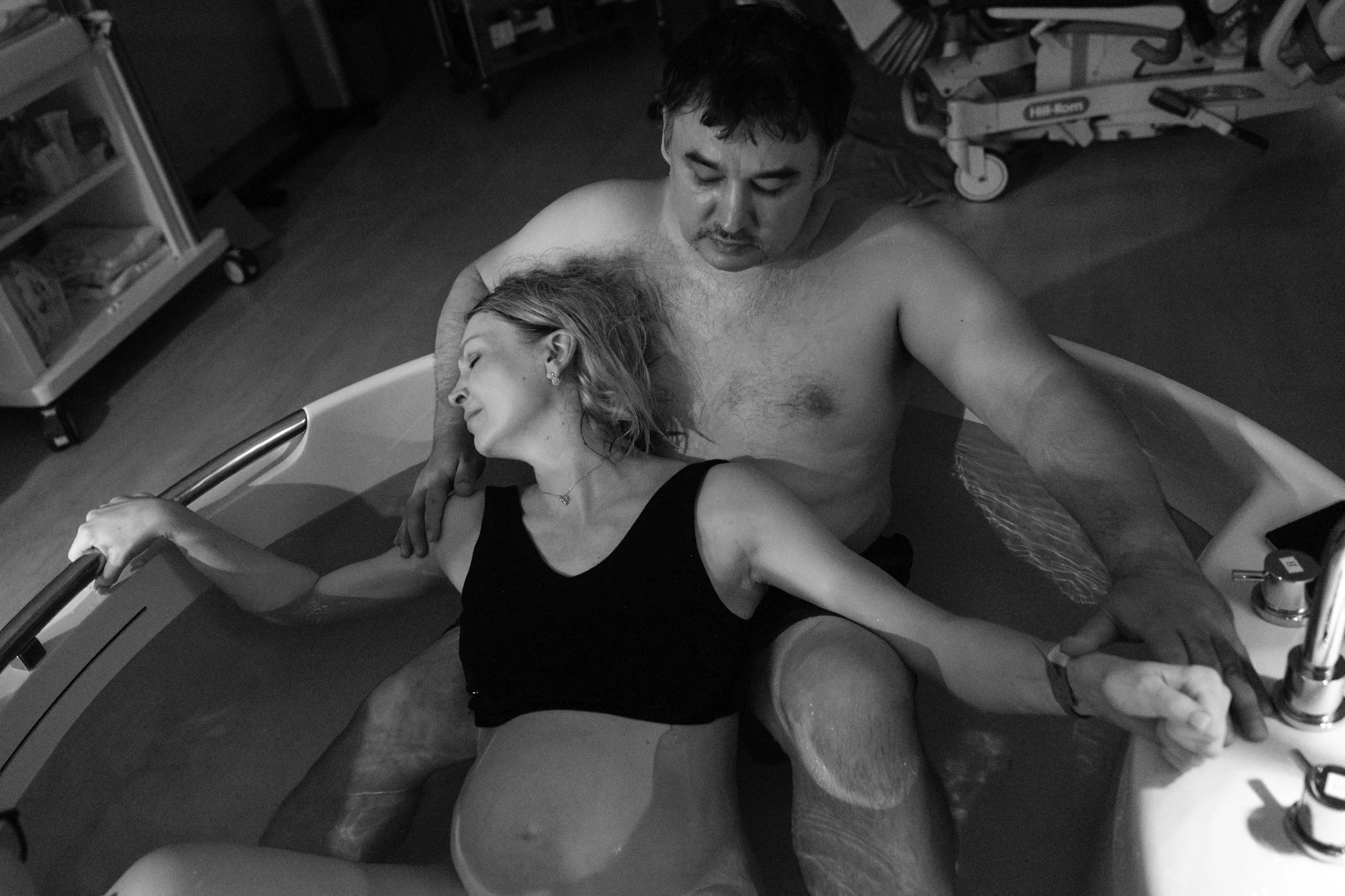 A black and white image of a woman focusing and pushing during a water birth at Dianthus in Taipei. She is in a birthing tub with her husband.