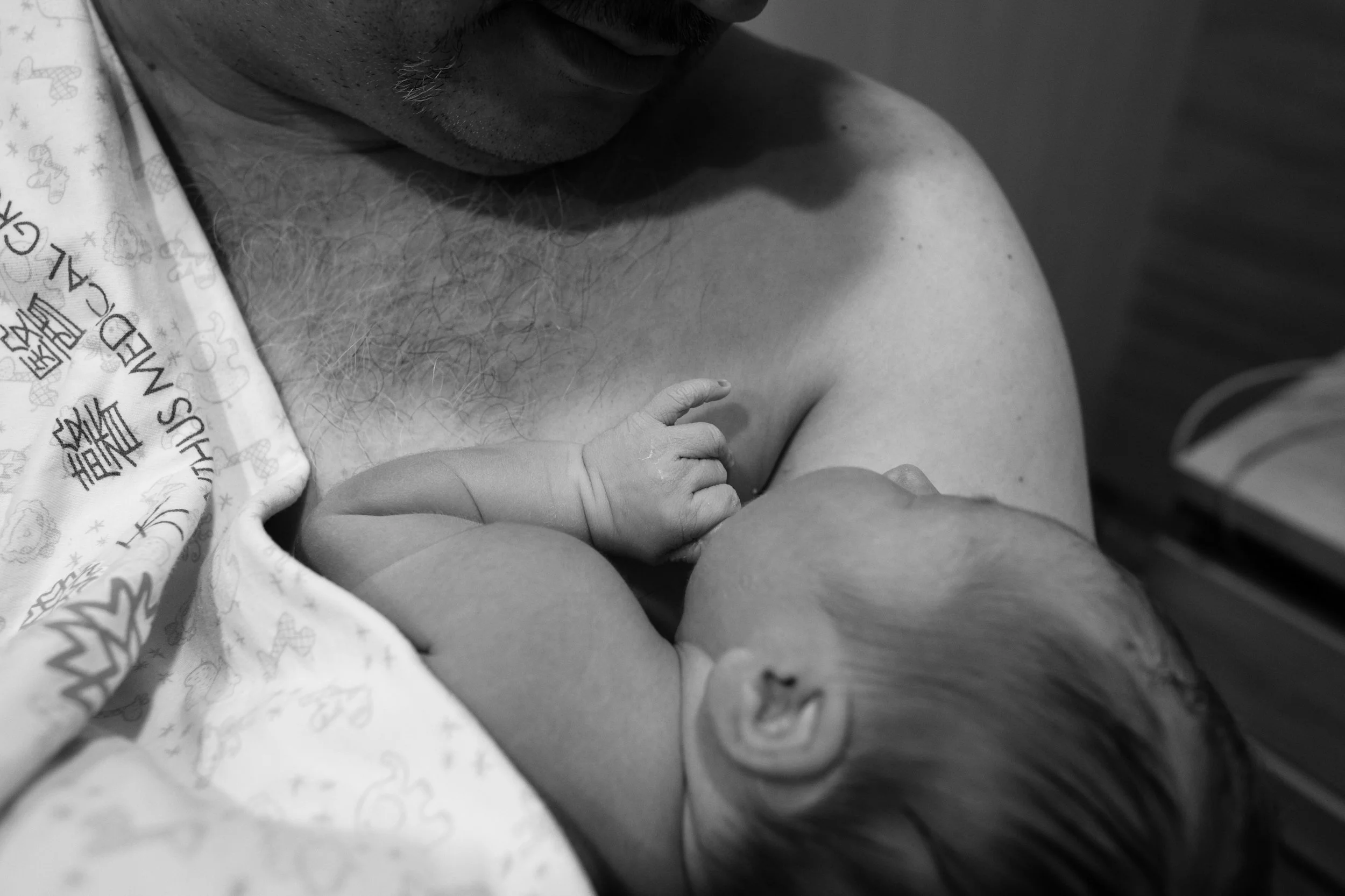 A black and white close-up photo of a newborn baby's hand on her father's hair chest. The father is doing skin-to-skin at Dianthus in Taipei.