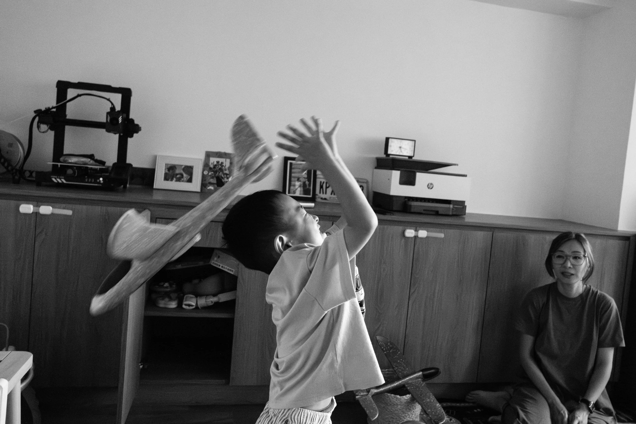 A black and white image of a little boy trying to catch an airplane that was thrown to him. The airplan slips past his outstretched hands. Photographed by Taiwan family photographer Cahleen Hudson.