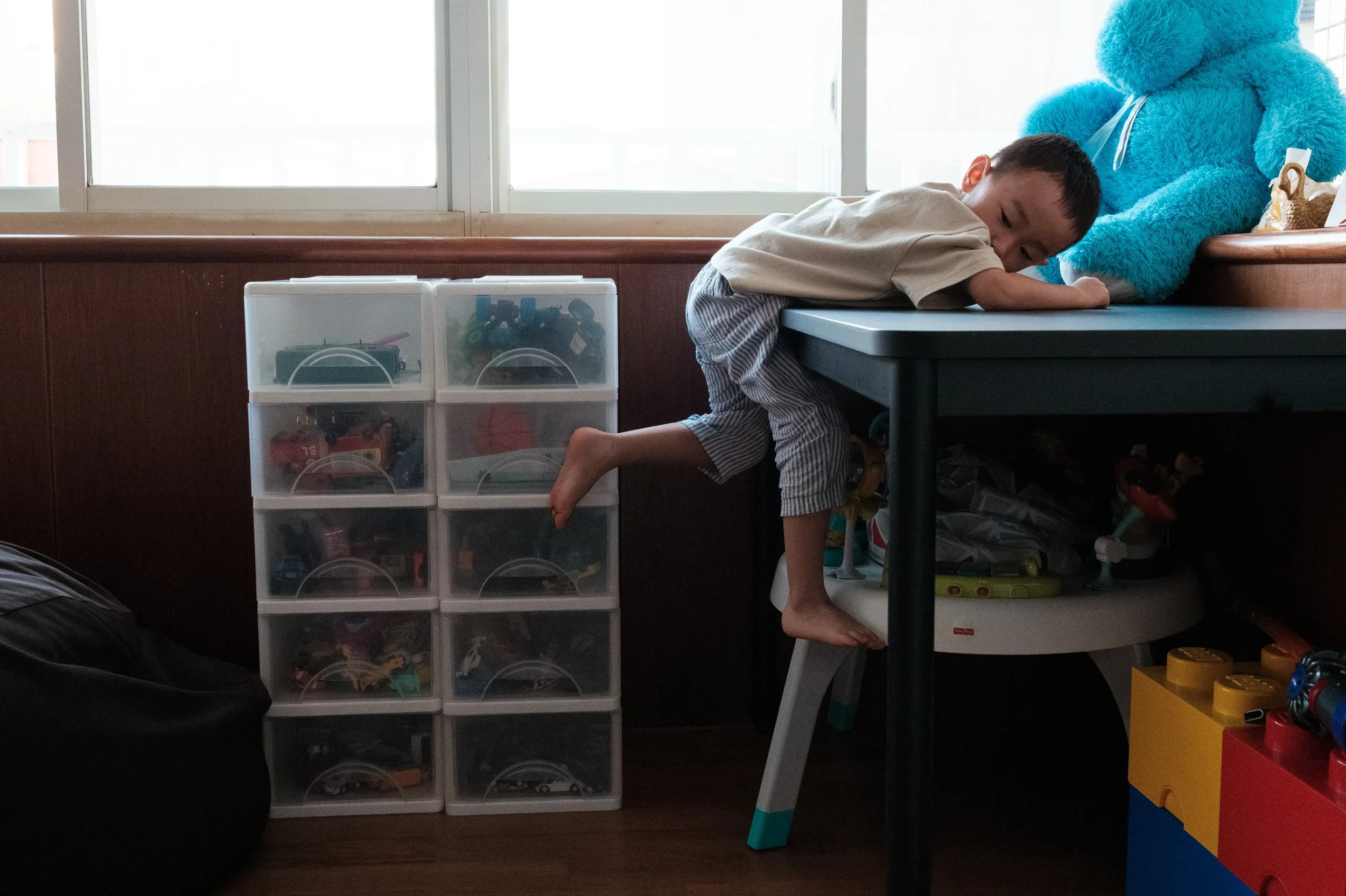 A color image of a boy climbing off a table. His legs are dangling as he tries to reach the floor. Photographed by Taipei documentary family photographer Cahleen Hudson.