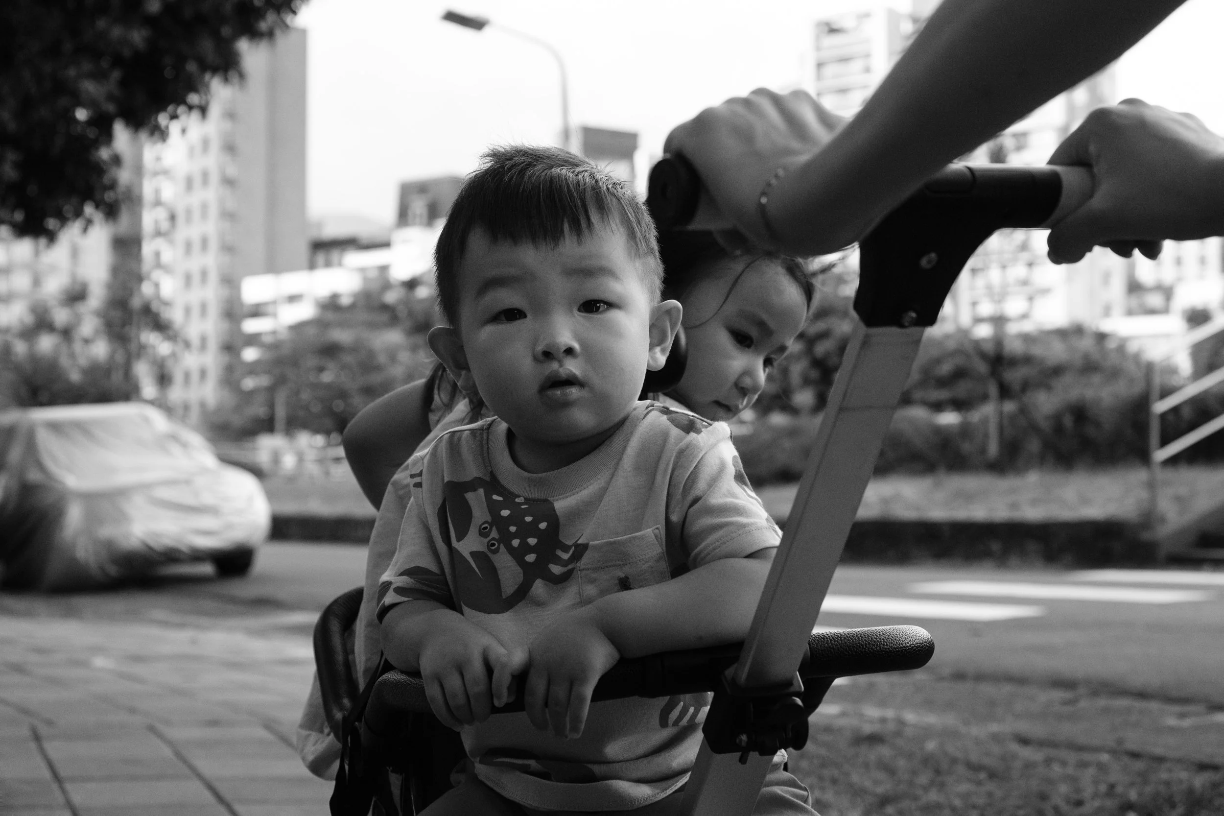 A black and white image of a little boy and a little girl being pushed in a stroller on a Taipei street. Photographed by family photographer Cahleen Hudson.