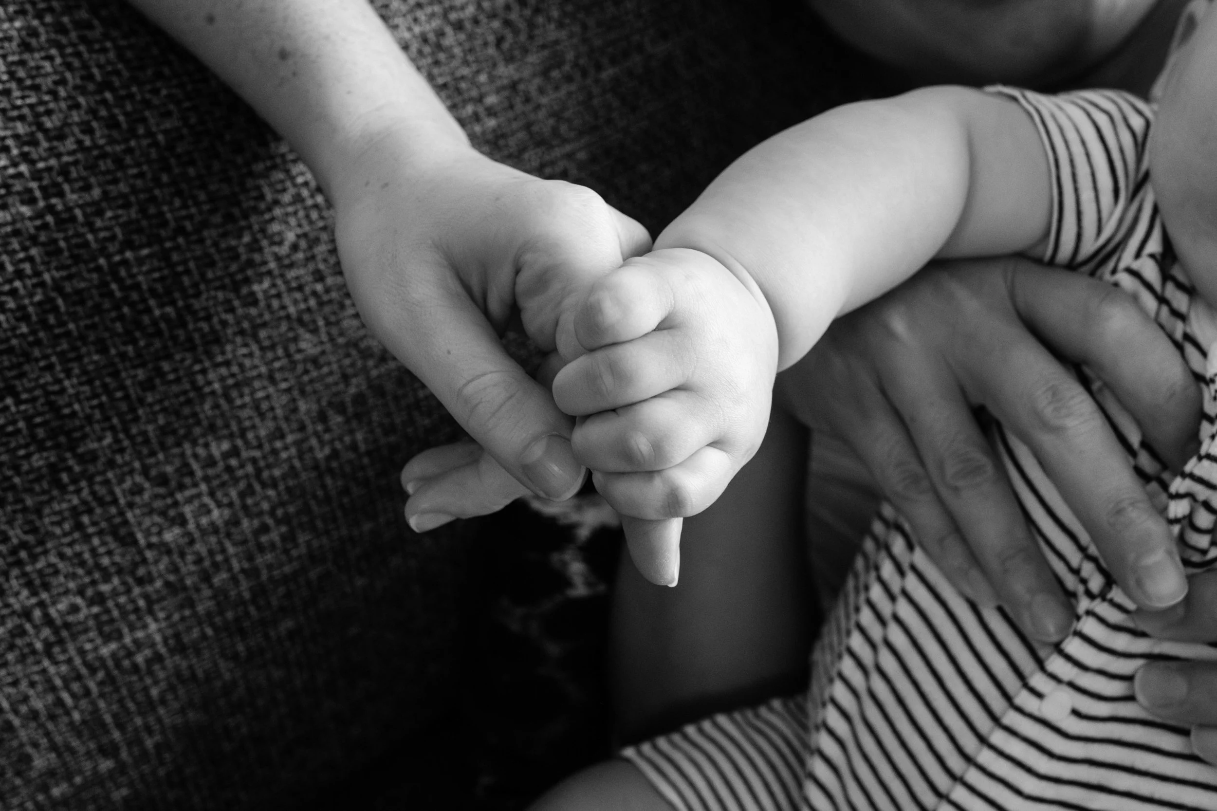 A close up black and white photo of a woman holding her baby's hand. The baby is only able to grasp one of his mom's fingers. Photographed by Taipei photographer Cahleen Hudson.