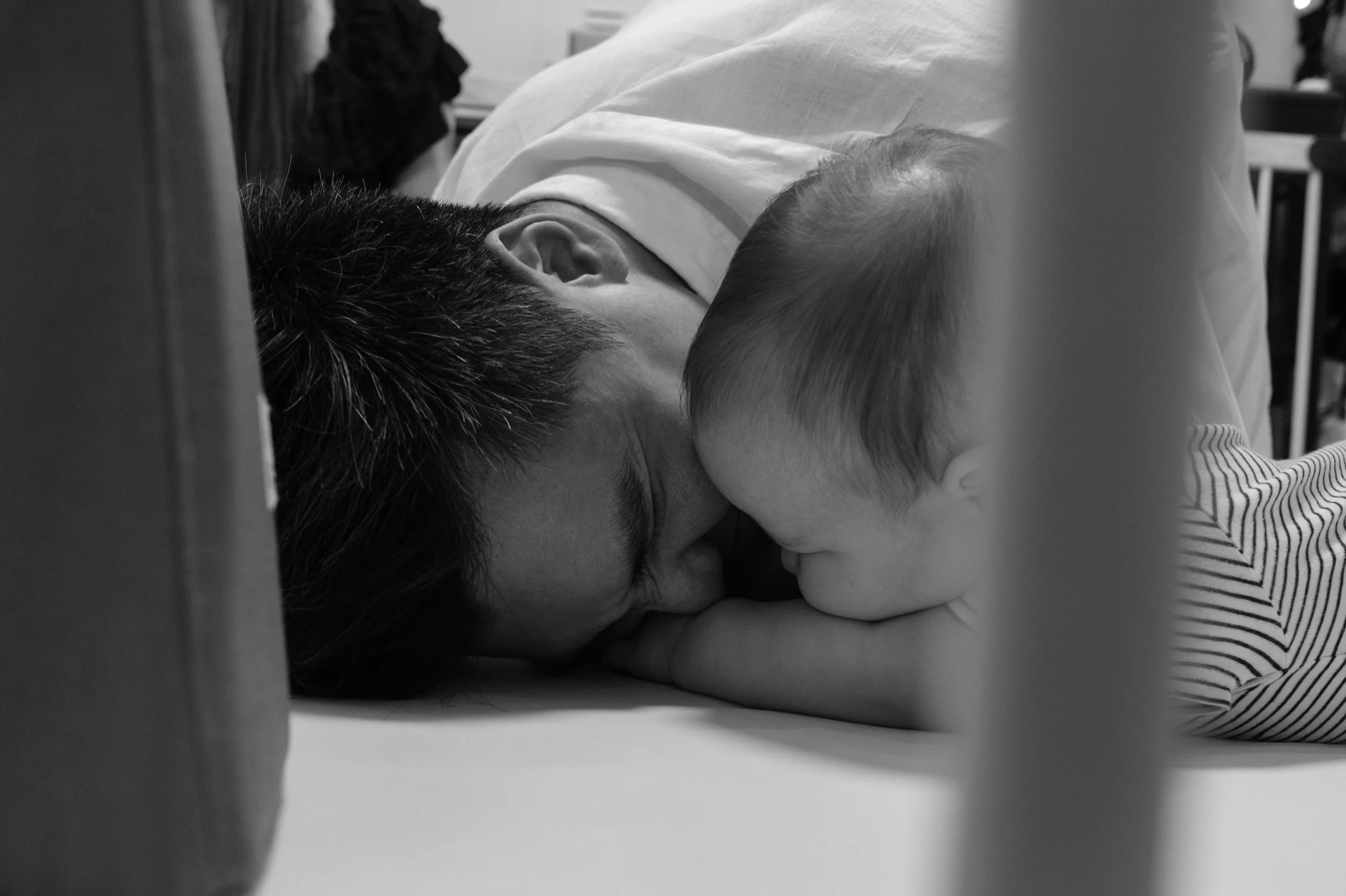 A black and white photo of a man touching his nose to his baby's nose while they're playing on the floor. Photographed during an at-home family photoshoot by Taipei photographer Cahleen Hudson.